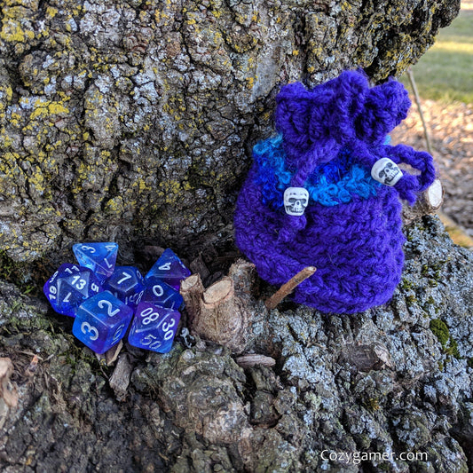 Handmade blue and purple crochet dice bag set beside matching dice on tree bark by CozyGamer.