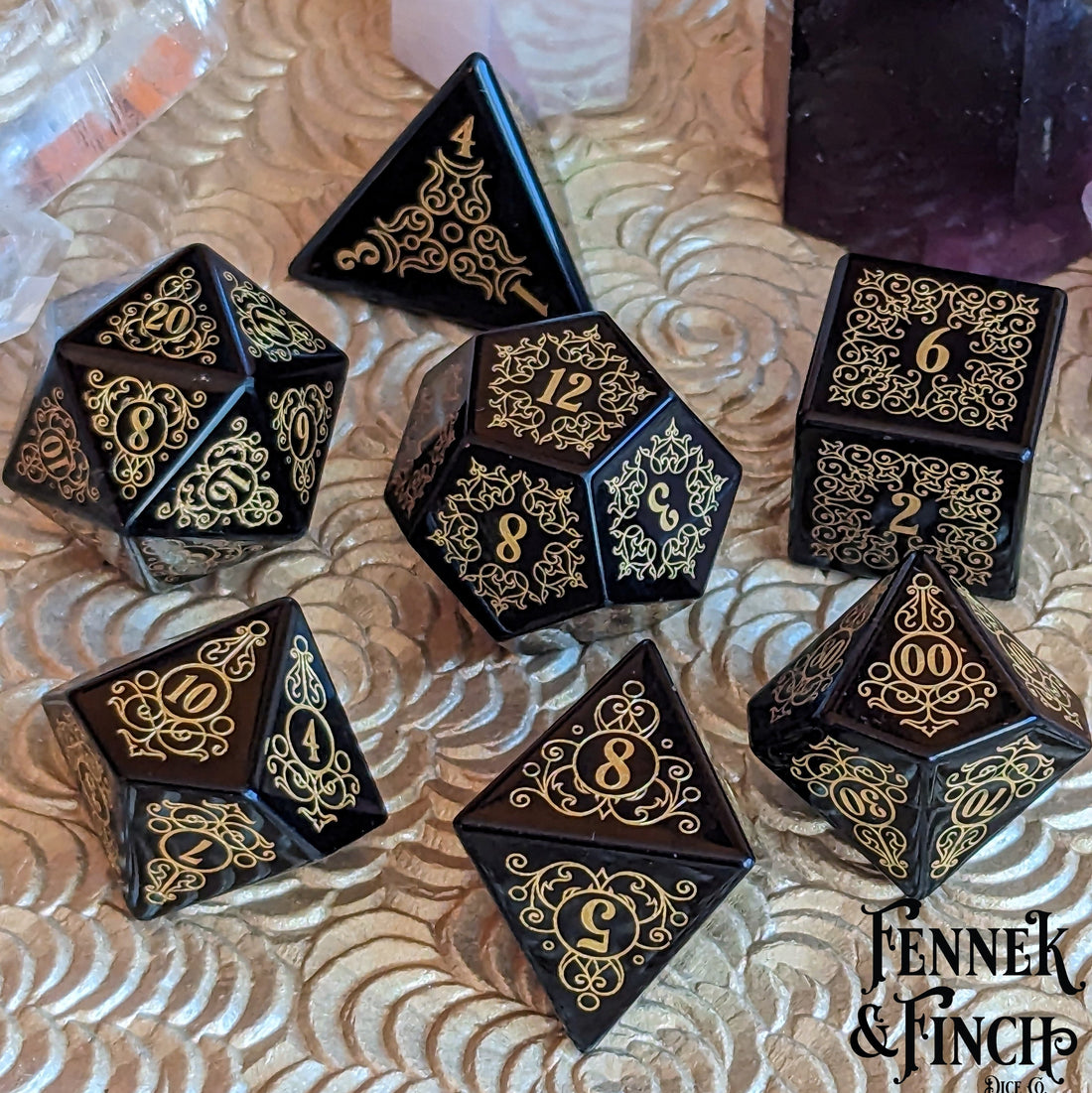 Black and gold engraved dice set on a decorative surface from Fennek & Finch, featuring intricate designs for tabletop gaming adventures.