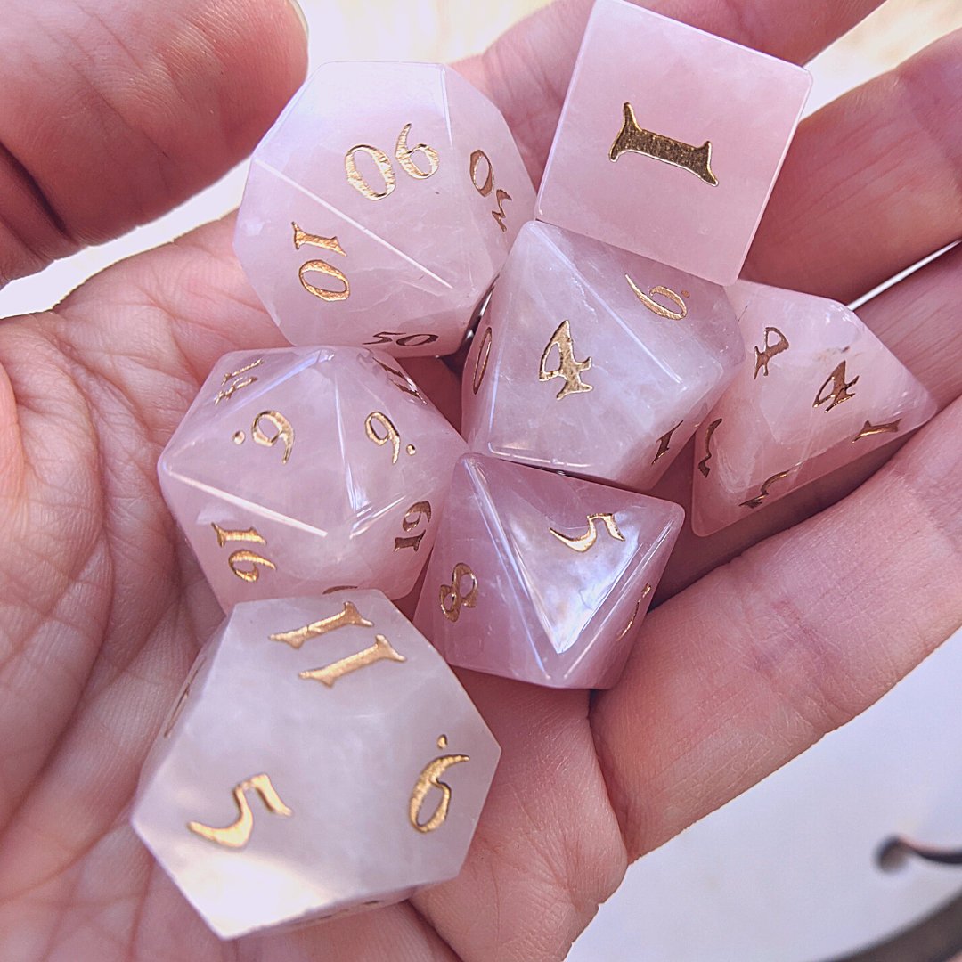 Rose Quartz gemstone dice set with gold numbers in a hand, perfect for DnD gaming and collectors.