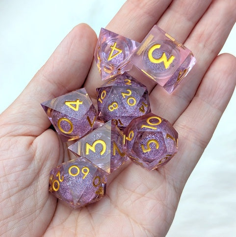 A set of translucent pink glitter polyhedral dice with gold numbers, held in a person's hand against a light background.