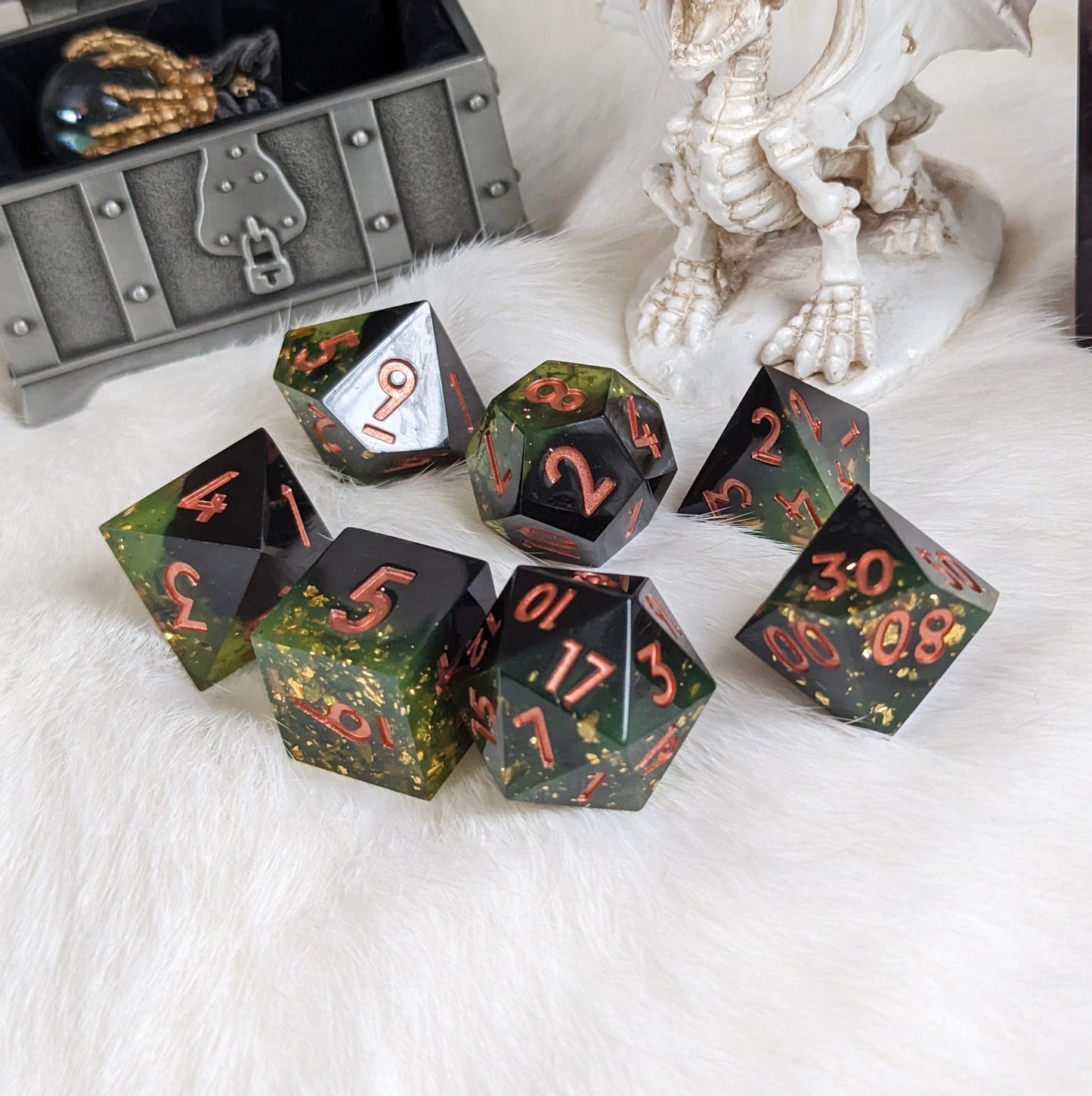 Dark green and black 7-piece sharp edge DnD dice set with copper font and gold flakes, placed on white fur background.