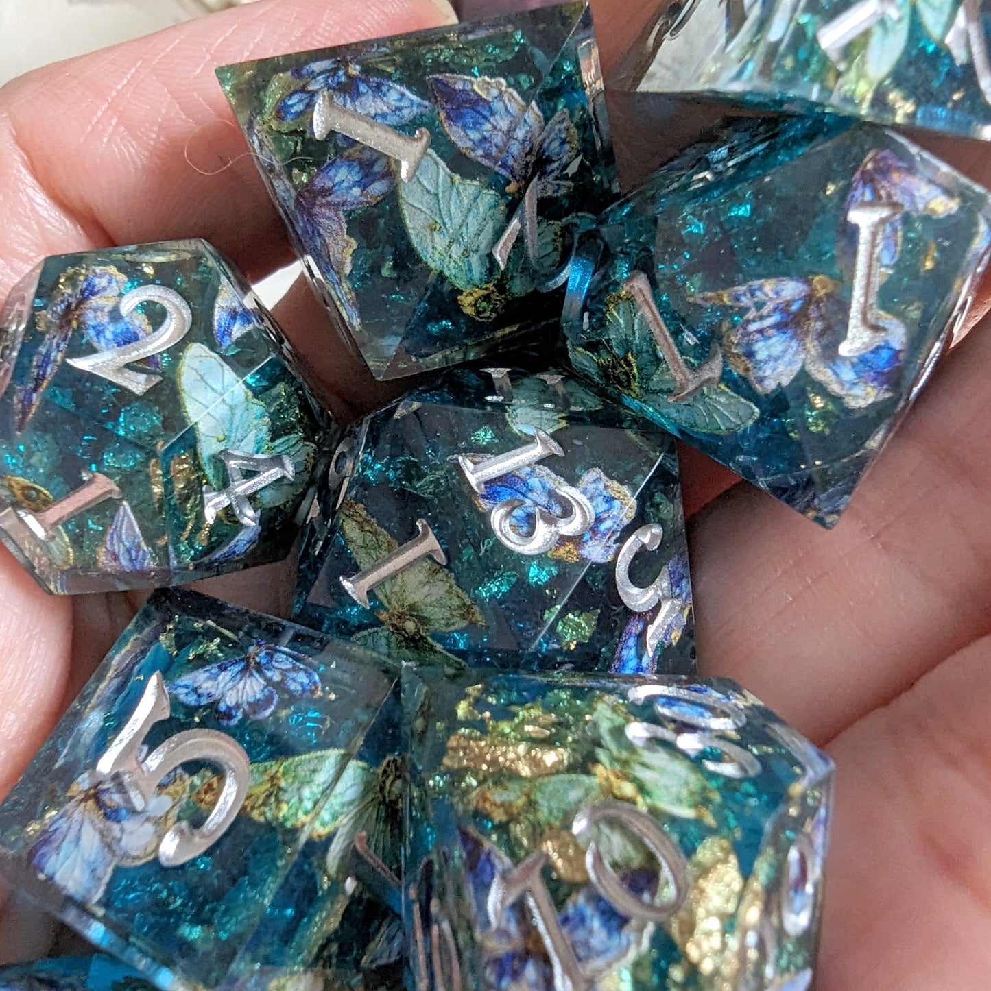 Enchanting Butterfly Realm DnD Dice Set with blue, gold, and purple designs in hand holding 7 unique TTRPG dice, silver font.