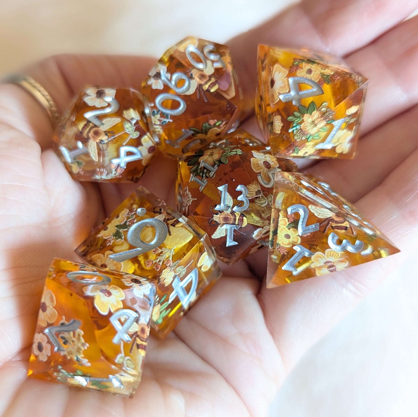 Honey Blossom Dice Set with floral designs, held in hand, showcasing intricate bee and flower details in golden honey color.