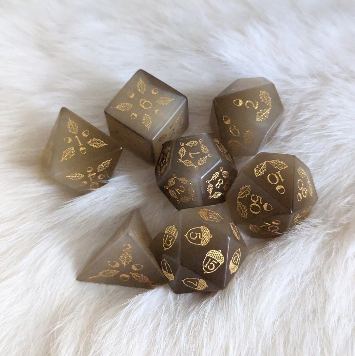 Light brown Cat's Eye dice set featuring acorn and oak leaf designs, perfect for gaming druids, displayed on a fluffy surface.