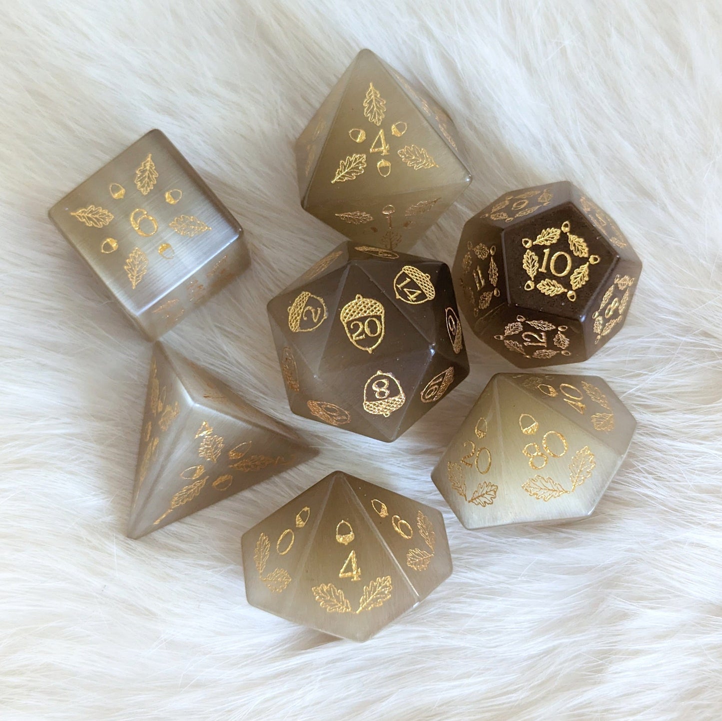 Acorn and Oak Light Brown Cat's Eye Dice Set featuring gold acorn and leaf designs on a soft surface.