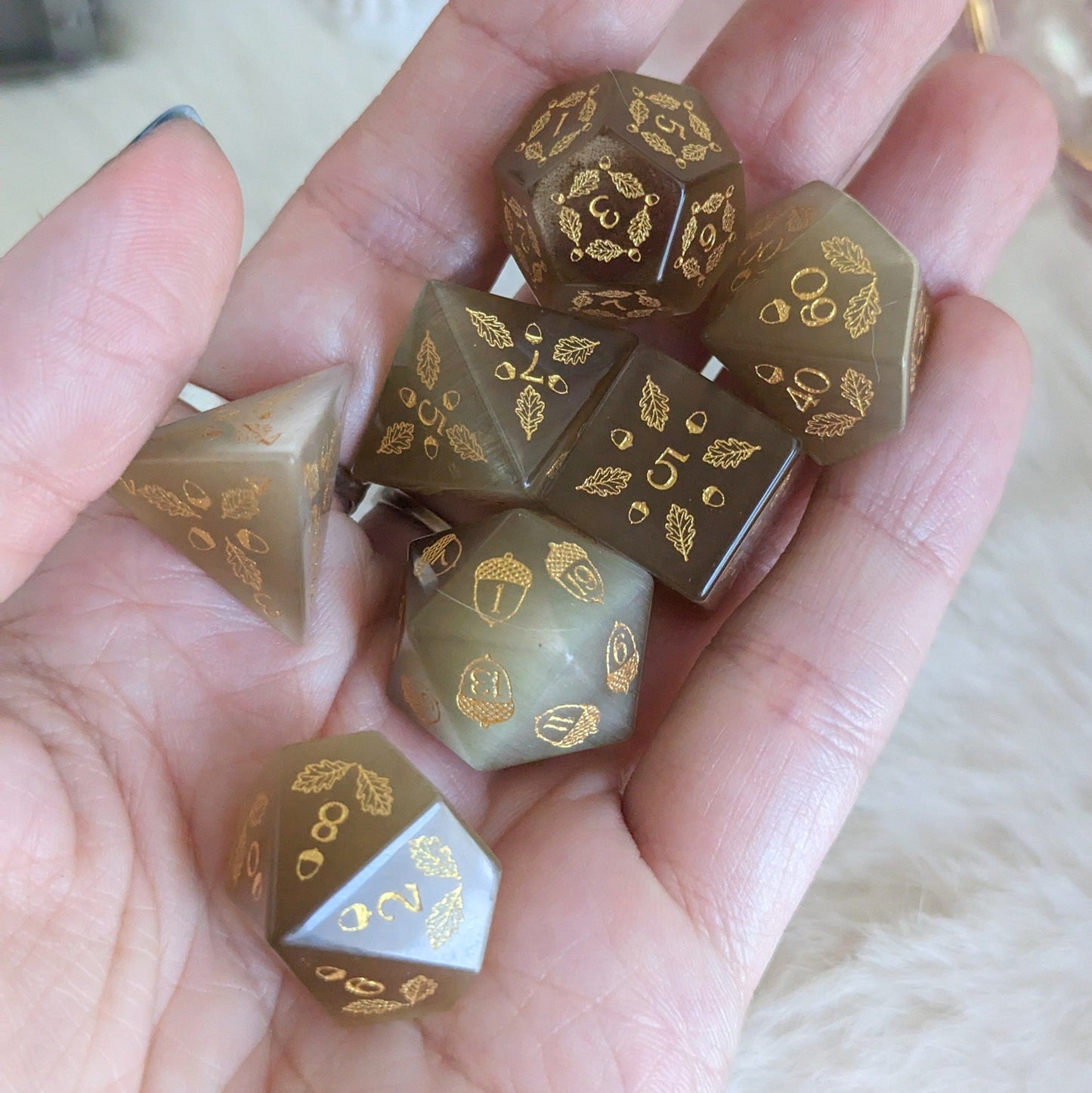 Acorn and Oak Light Brown Cat's Eye Dice Set with acorn and oak leaf designs held in a hand, perfect for gaming druids.