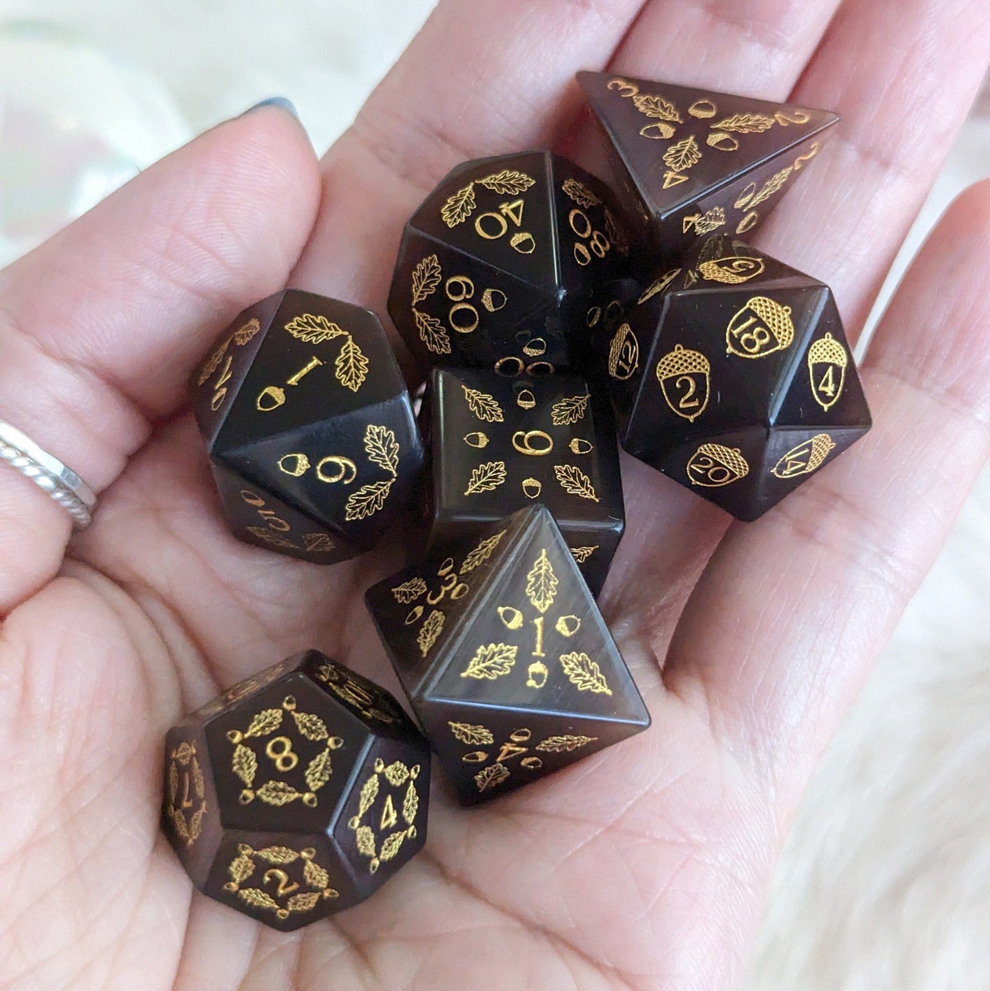 Hand holding Acorn and Oak Dark Brown Cat's Eye Dice Set with detailed acorn and oak leaf designs, perfect for gaming druids.