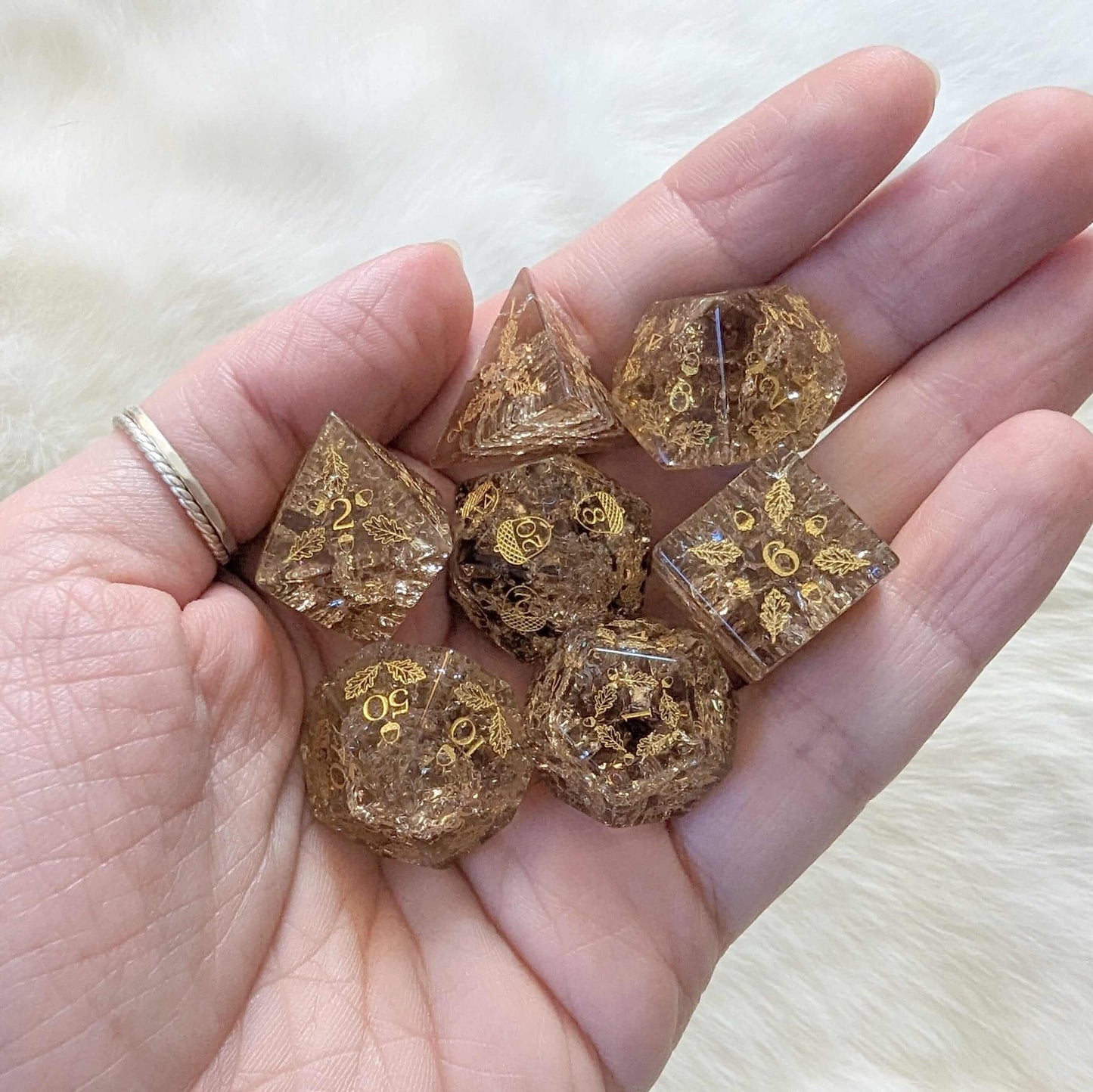 Hand holding Acorn and Oak Brown Lightning Glass Dice Set with acorn and oak leaf design, featuring seven polyhedral dice.
