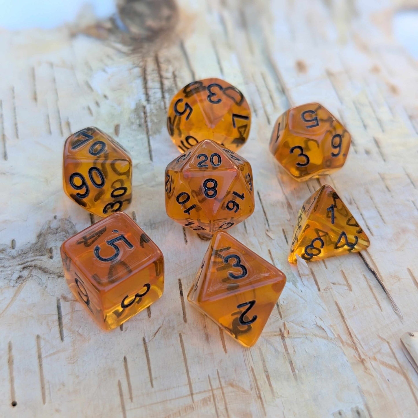 Amber Gems Dice Set with clear brown hue and black numbers for TTRPG like Dungeons & Dragons on wooden surface