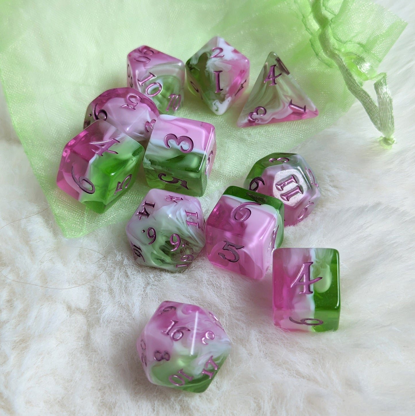 Bardic Inspiration Dice Set with 11 TTRPG dice in pink, white, green colors, metallic magenta font, on a soft background.