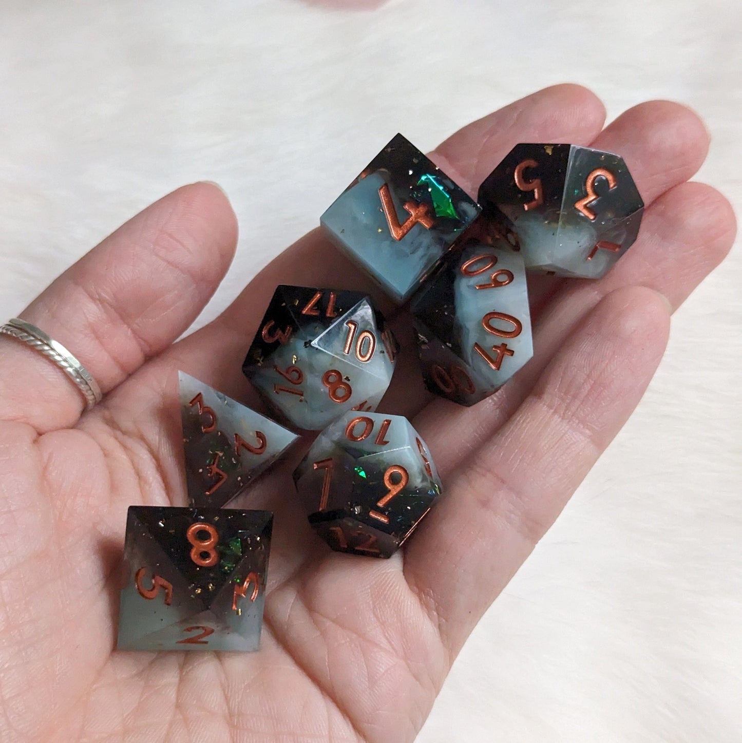 Hand holding 7-piece black and white layered DnD dice set with copper numbering, perfect for TTRPG sessions.