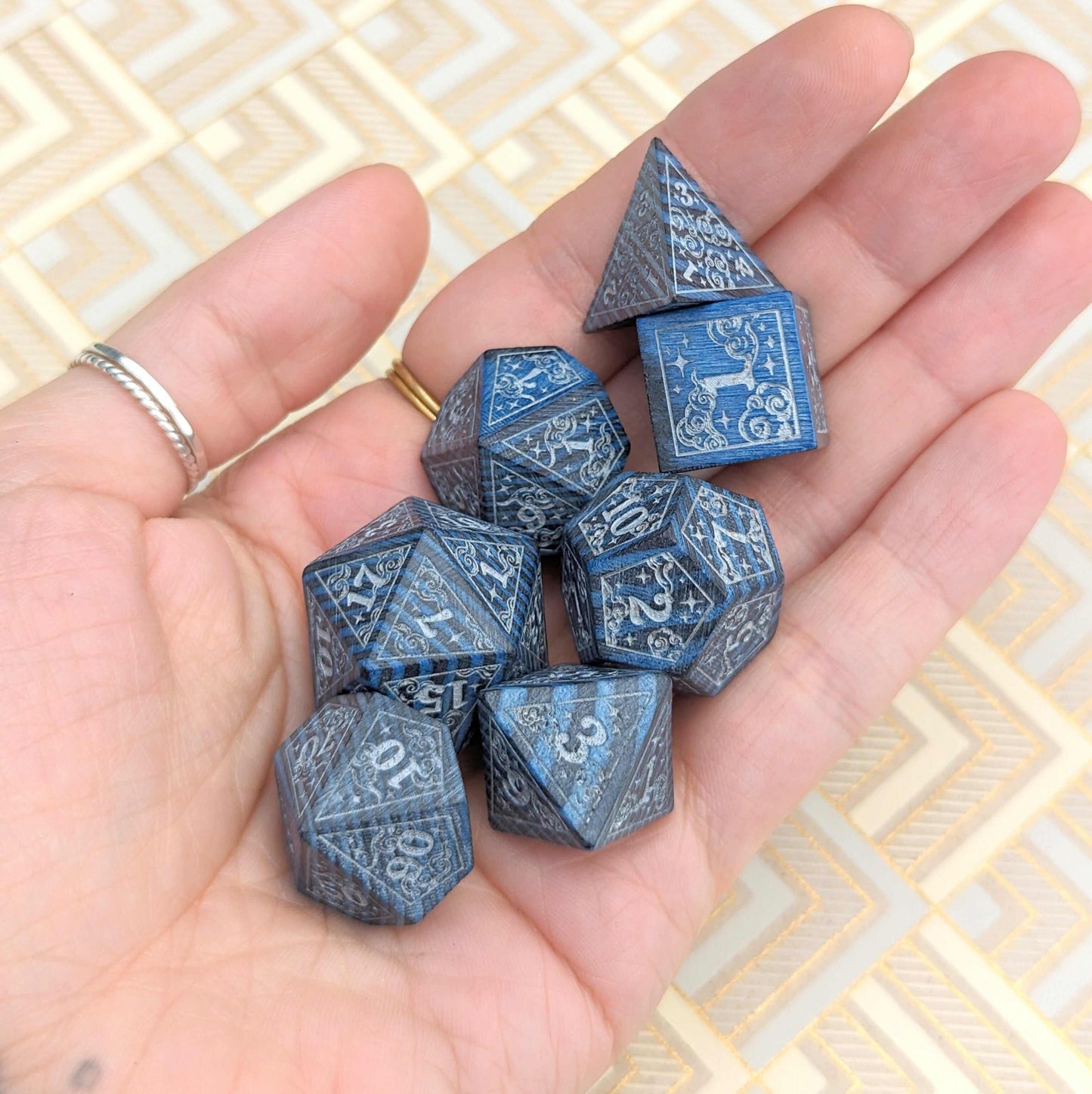 Person holding a Blue Dreamy Star and Moon Wood Dice Set with intricate designs for Dungeons & Dragons gameplay.
