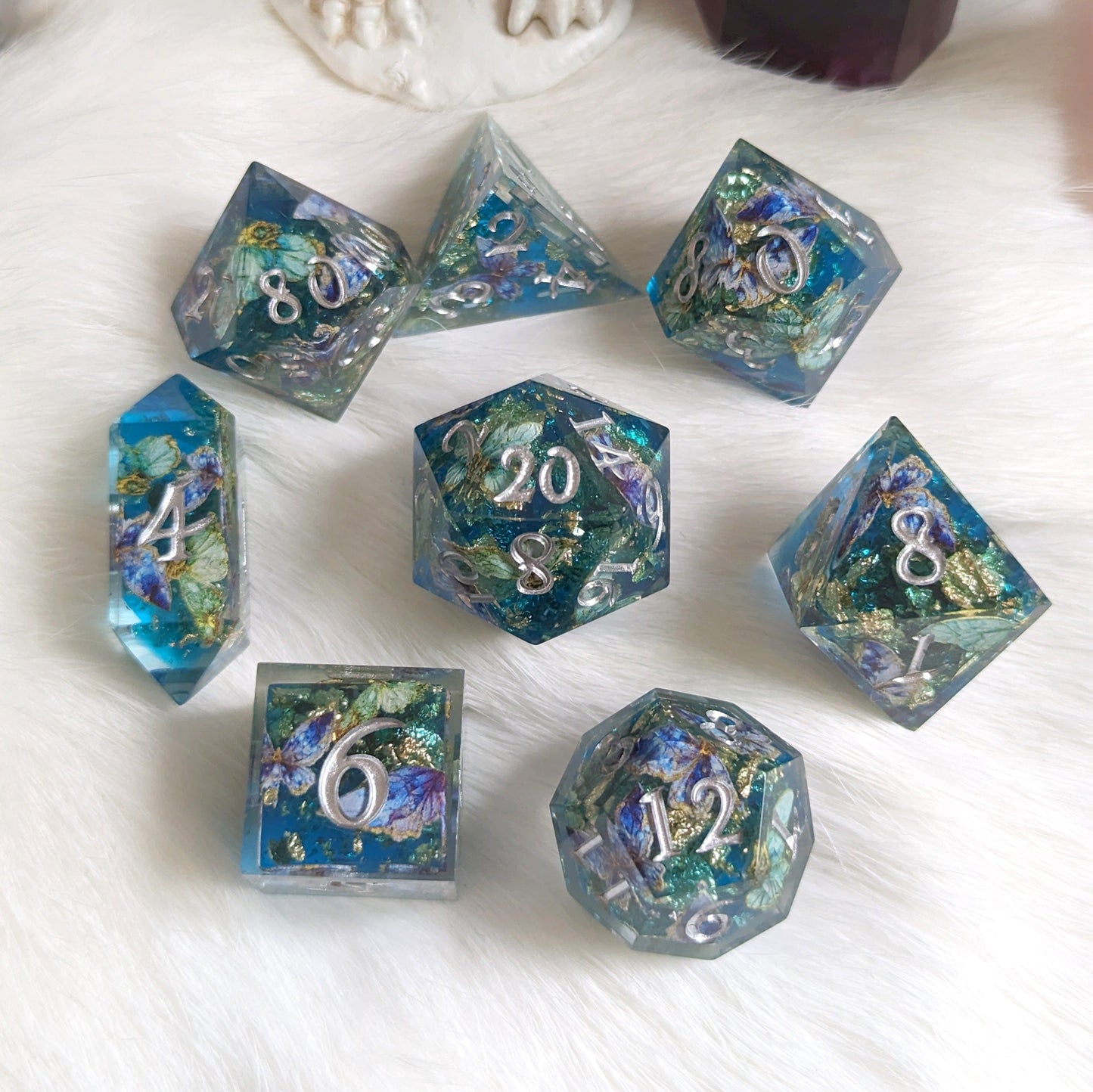 Butterfly Realm DnD Dice Set with purple butterfly accents, featuring a blue and gold core and silver font, arranged on a white surface.