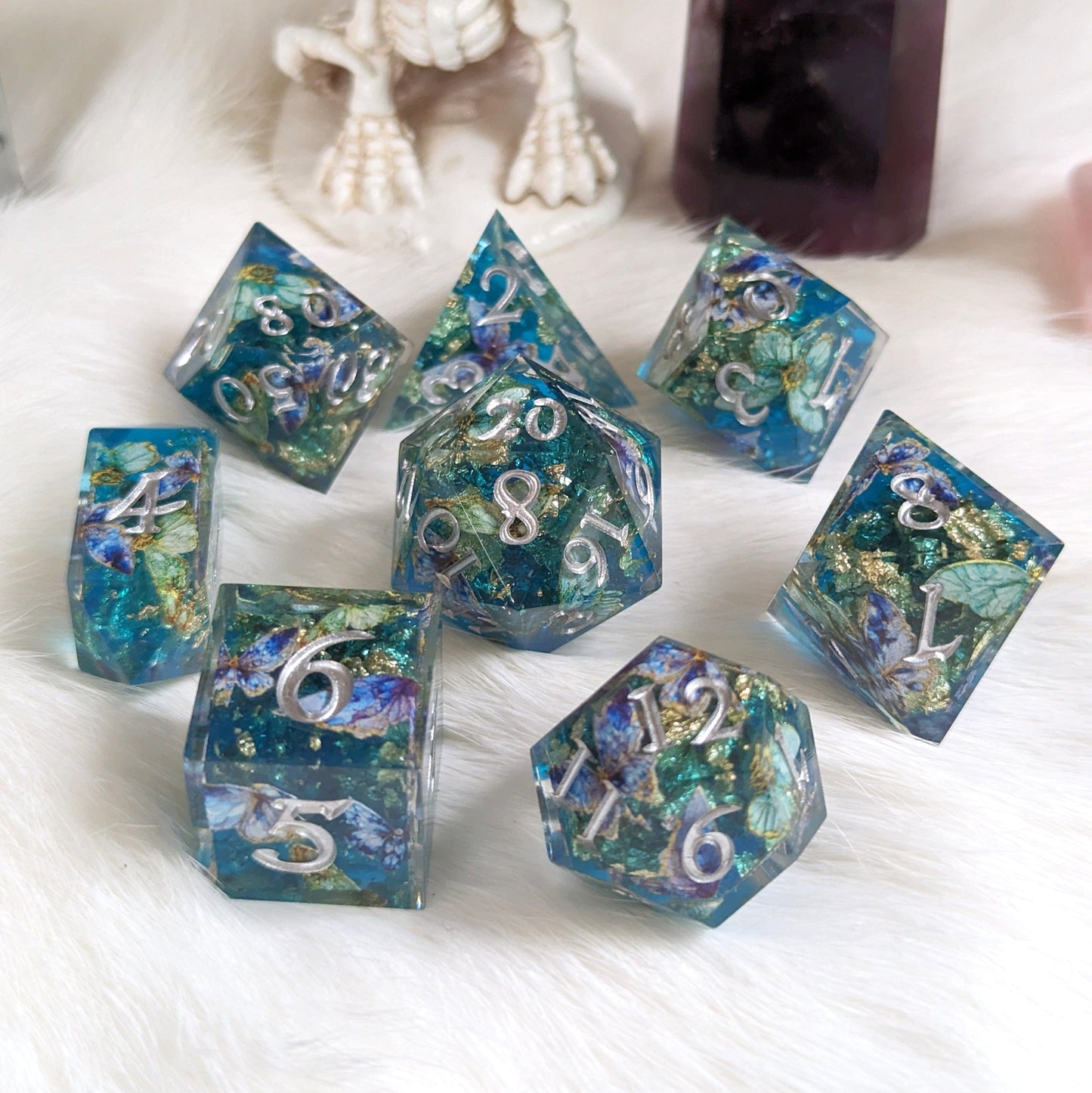Butterfly Realm DnD Dice Set with blue and gold core, purple butterflies, and silver numbers, 8 dice displayed on a fluffy surface.