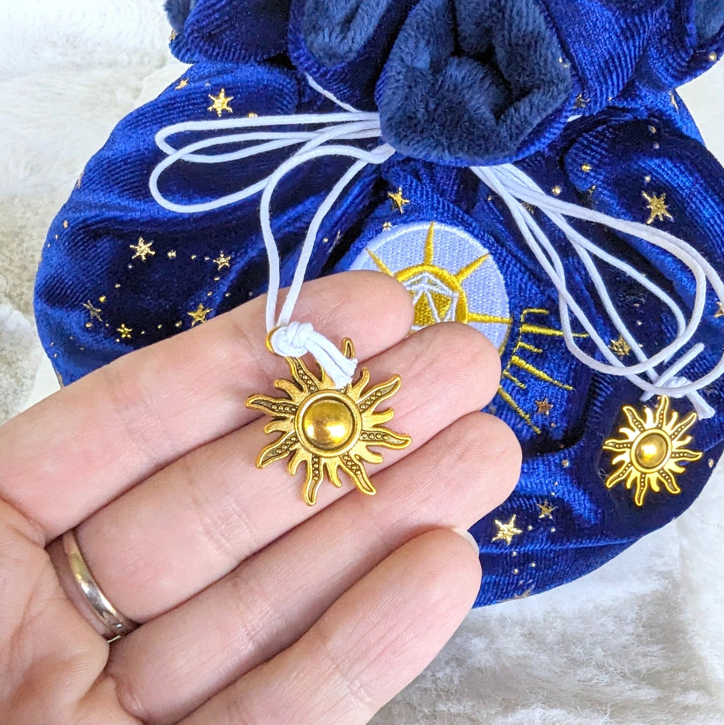 Starry blue cleric dice bag with gold sun charm drawstring and embroidered D20 mace design.
