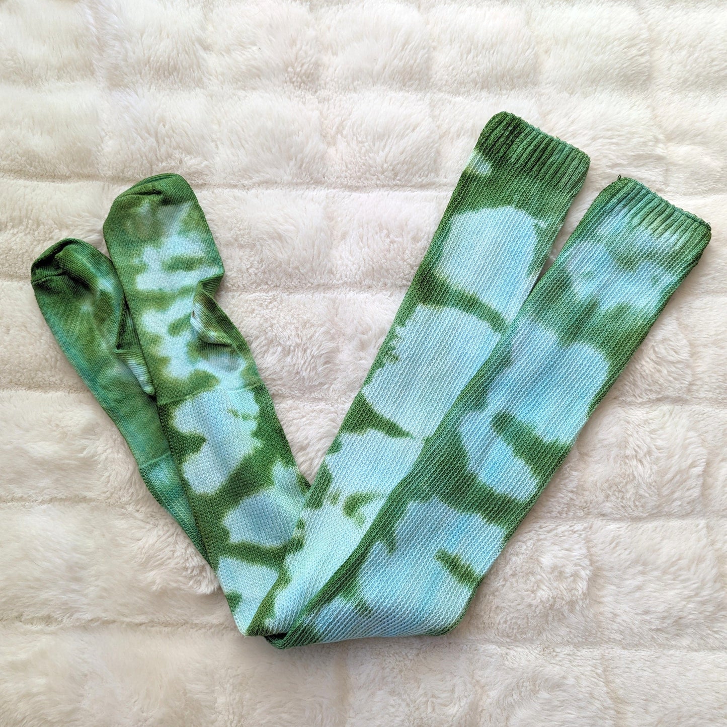 Tie-dyed blue-green cotton thigh-high socks on a soft cream background