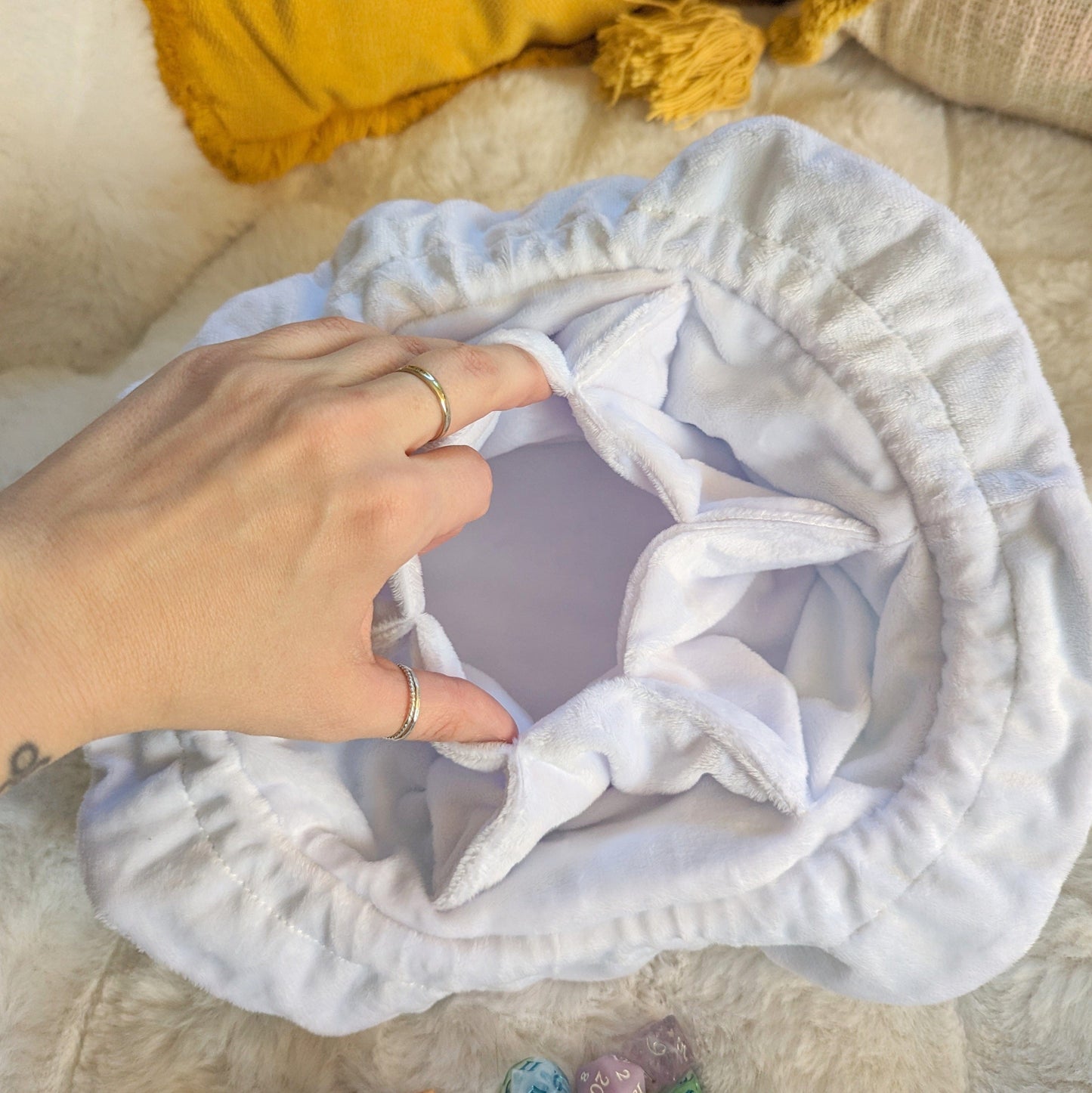 Hand holding open white plushy multi-pocket dice bag interior view on soft cushion.