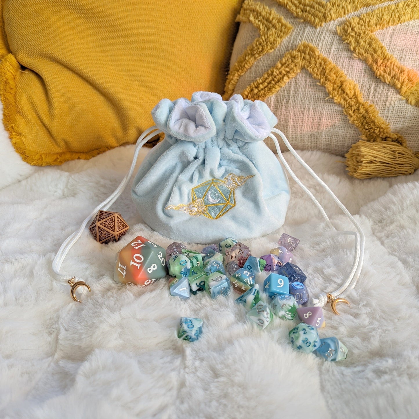 Blue multi-pocket dice bag with D20 cloud embroidery, crescent moon and star, adorned with gold beads and filled with colorful dice.