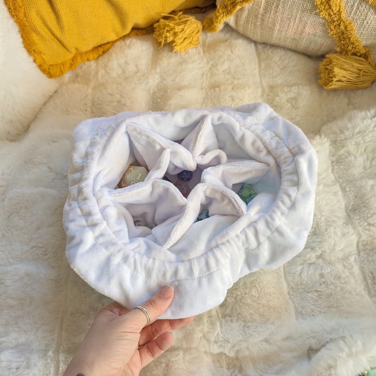 Hand holding a blue multi-pocket dice bag with plush fabric, open to show dice inside.