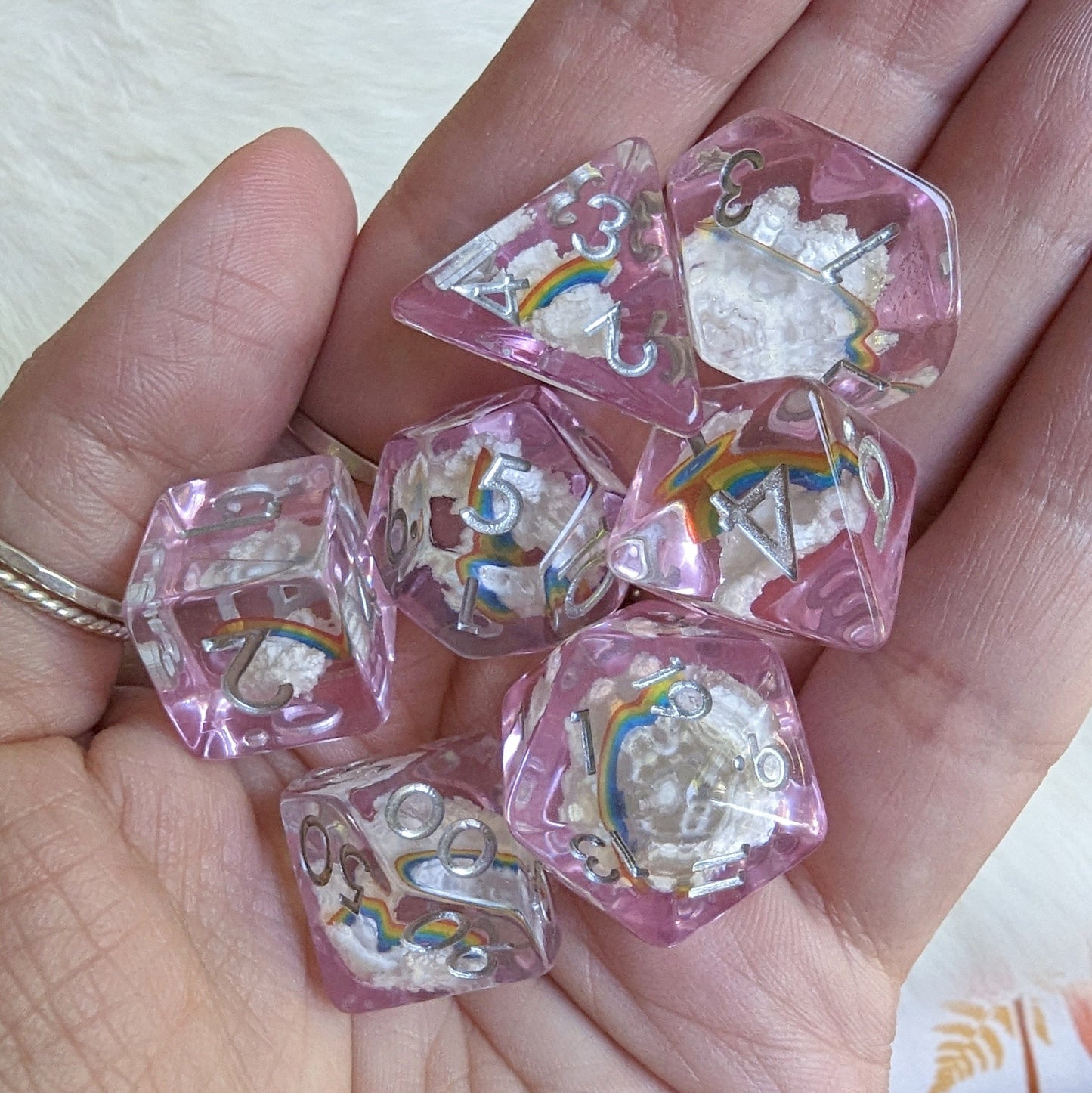 Hand holding Dreamy Rainbows and Clouds dice set with purple resin, white clouds, and colorful rainbows.