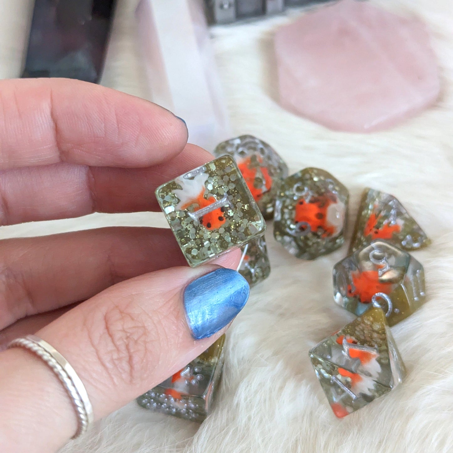 Hand holding Fancy Goldfish Dirty Pond Dice Set with orange goldfish in resin and green glitter, perfect for tabletop games.
