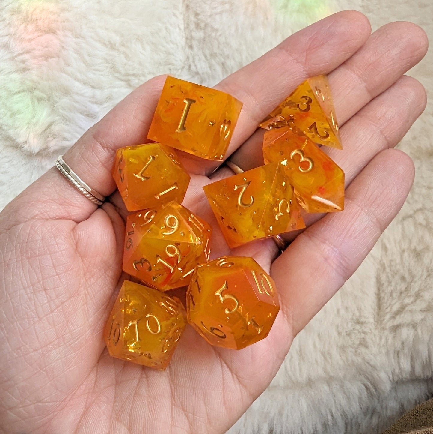 Flame Cast DnD Dice Set with gold numbers in red, yellow, and orange hues, displayed in a hand on a soft background.