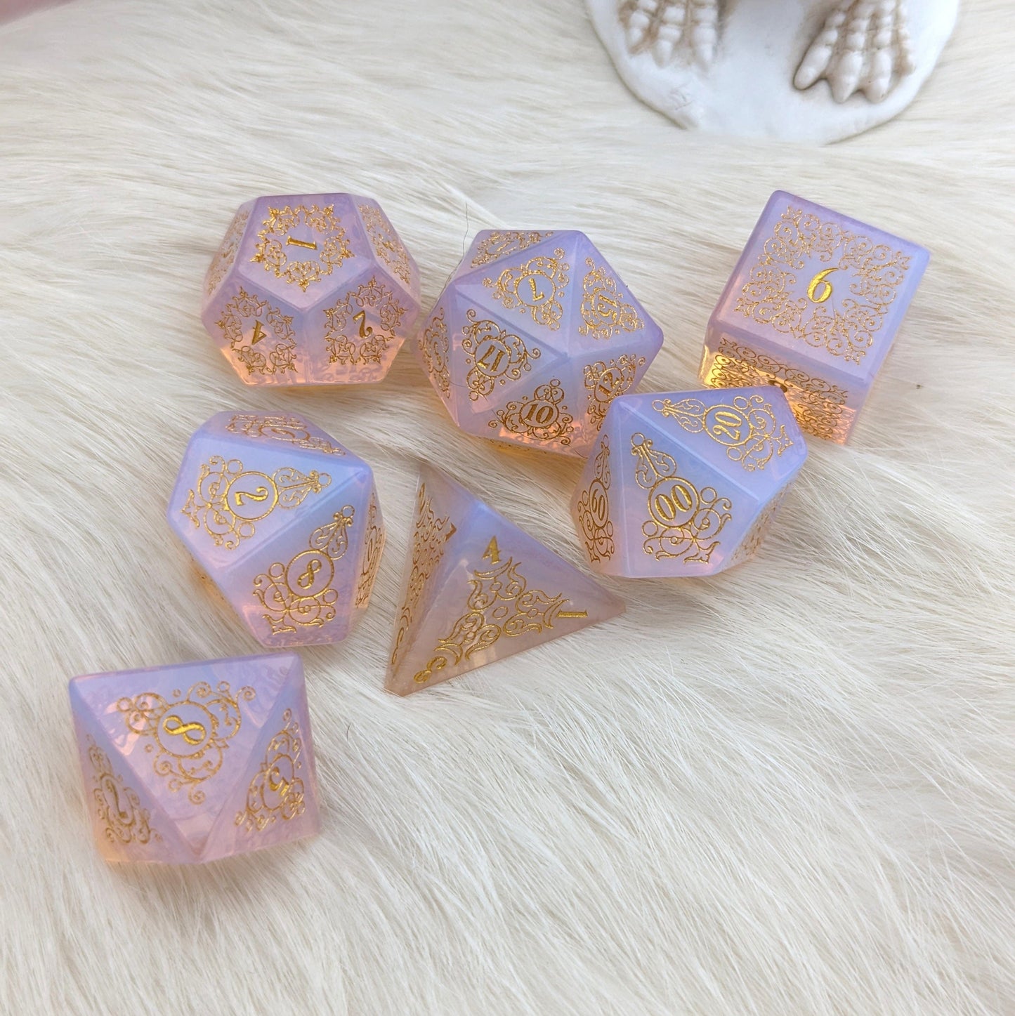 Garden Gate glowing pink opalite gemstone dice set with intricate floral and swirl designs on a soft white fur background.
