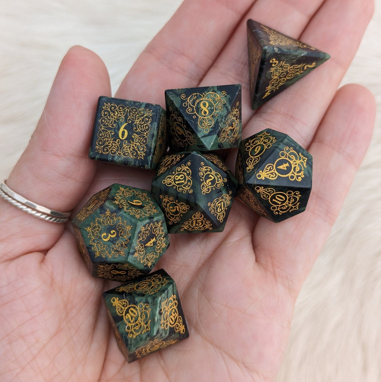 Hand holding Garden Gate Jasper Gemstone Dice Set with intricate green jasper and gold design.