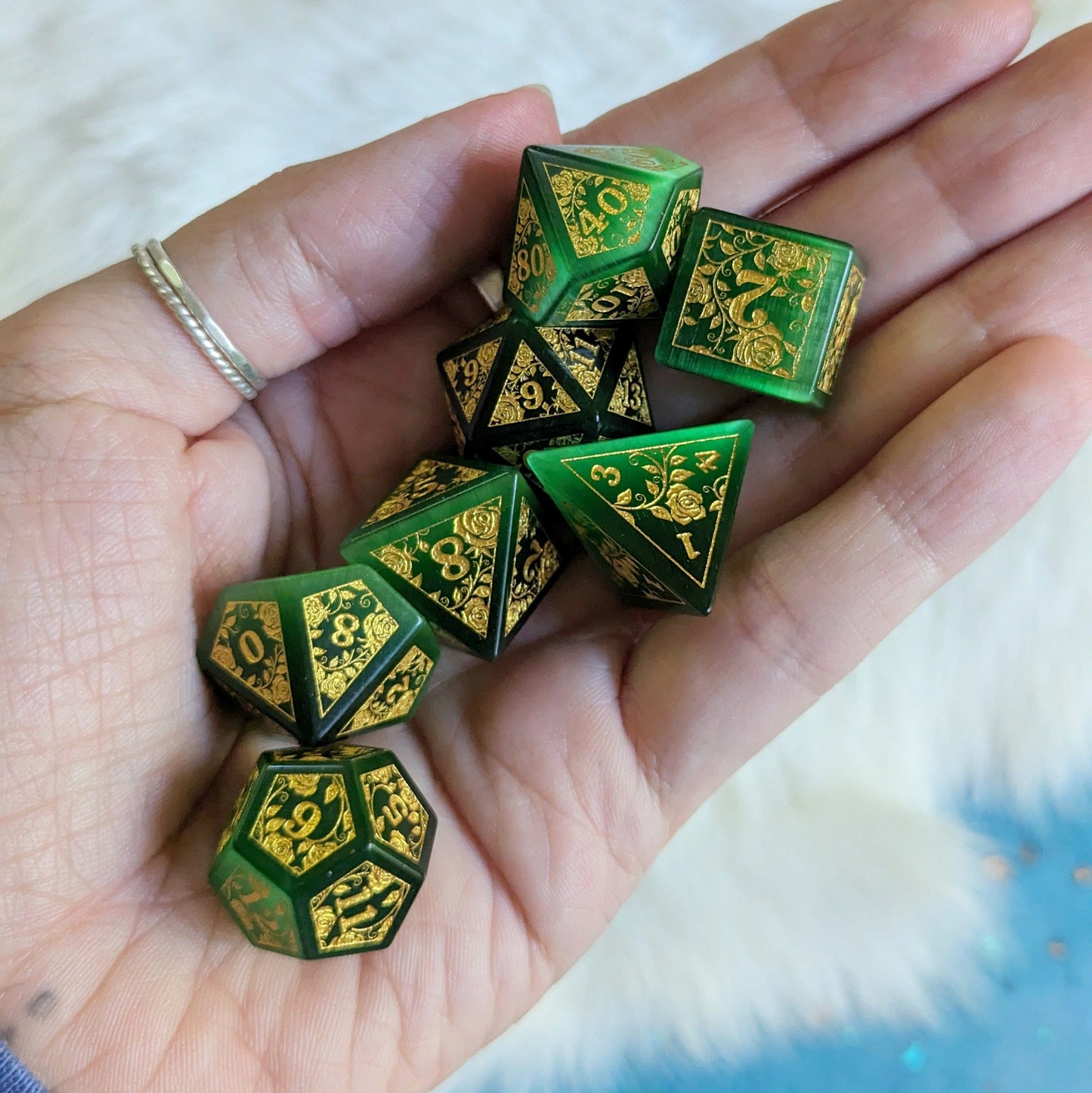 Hand holding green cats eye rose engraved dice with gold vine design, perfect for Dungeons & Dragons gaming sessions.