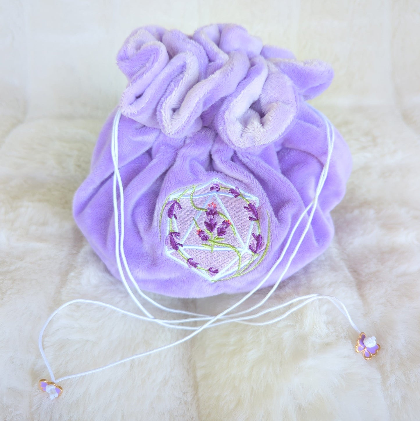 Lavender dice bag with multi pockets, featuring a D20 design and lavender blooms, purple drawstrings, and butterfly charms.