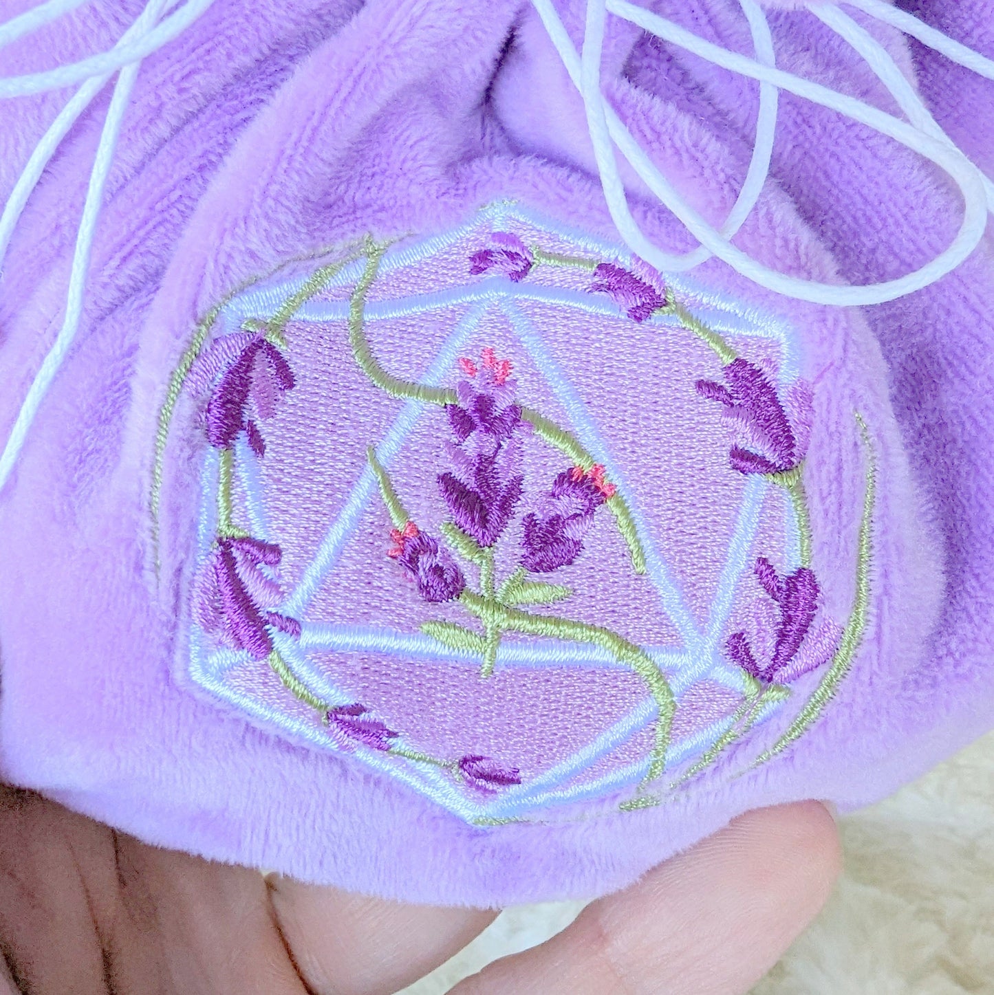 Lavender dice bag with embroidered D20 and floral design, purple plush fabric, strong drawstrings, and butterfly charms.