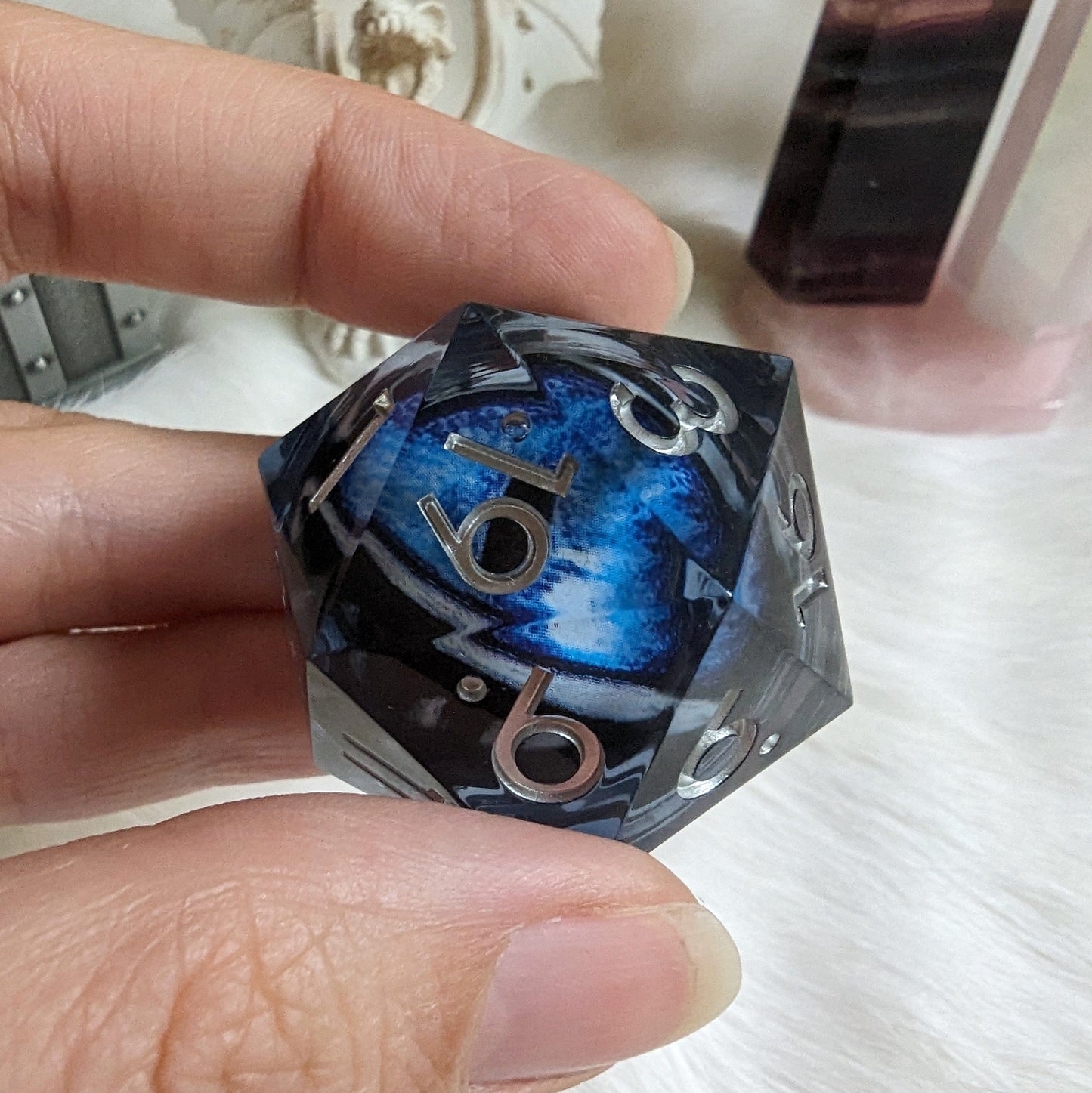 Hand holding a blue and black liquid core eye D20 die with glitter, designed for Dungeons and Dragons tabletop games.