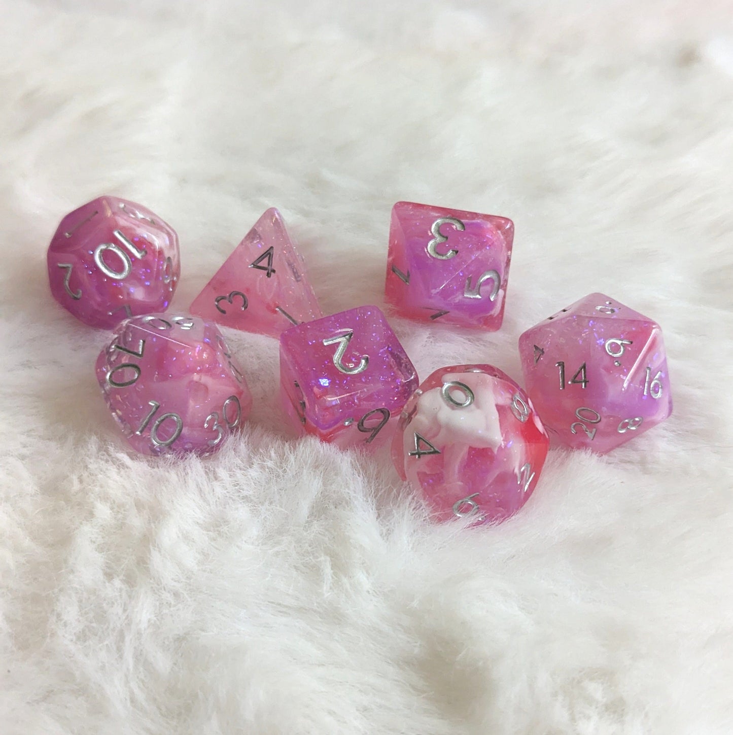 Purple, red, and pink Lover's Enchantment Dice Set with glitter, perfect for enhancing tabletop RPG sessions on a fluffy surface.