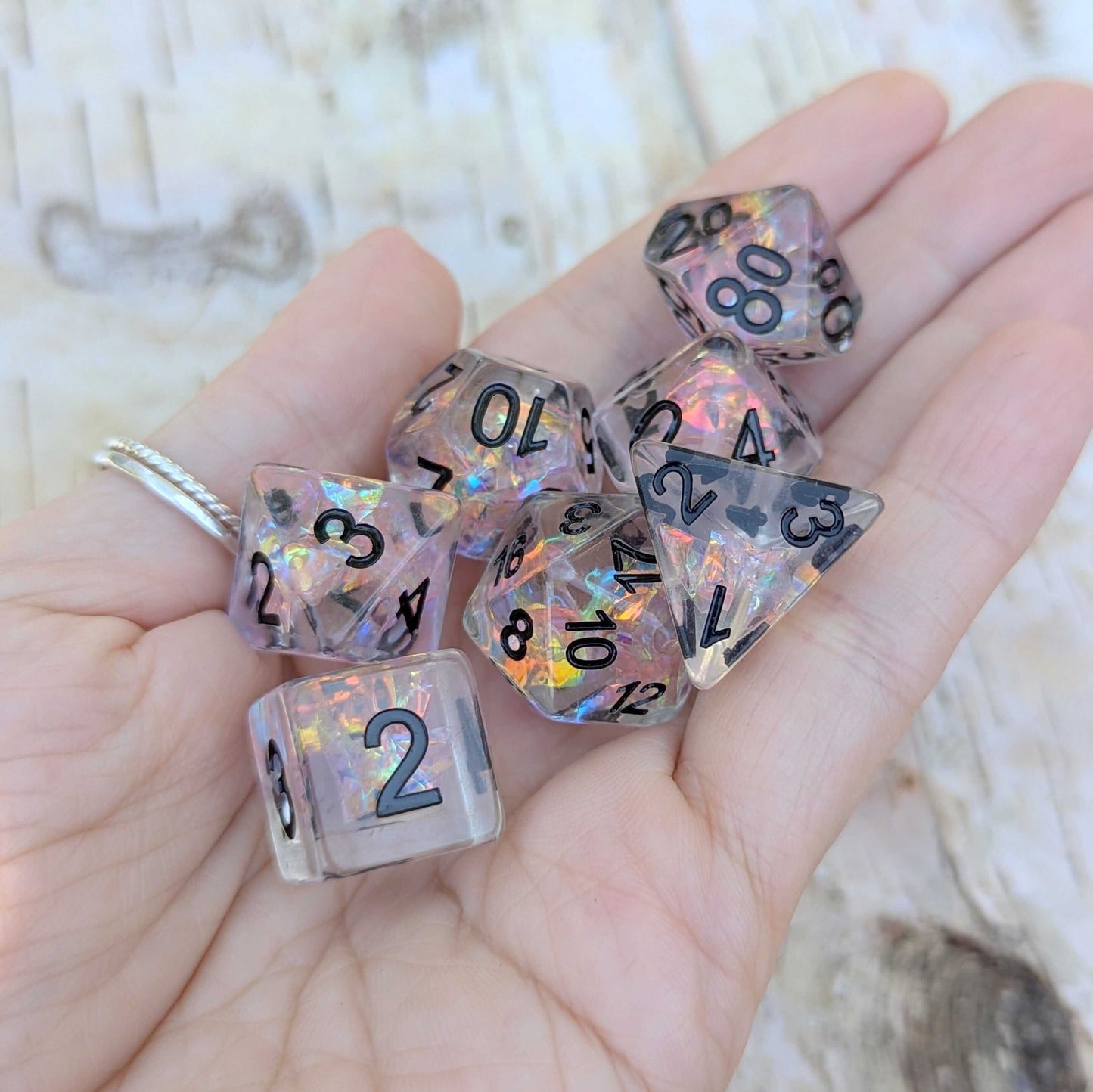 Hand holding Moonlight Fantasy TTRPG Dice Set with pink iridescent cellophane and black font.