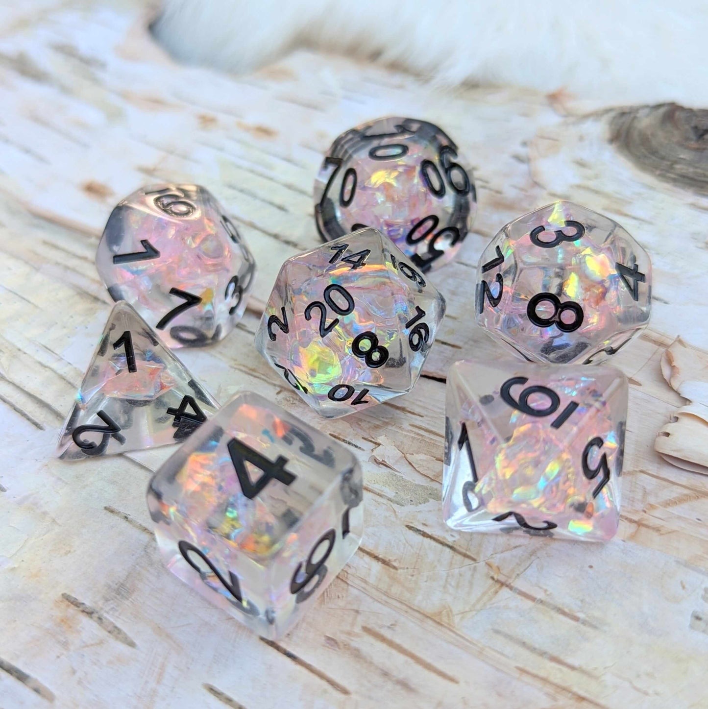 Moonlight Fantasy TTRPG Dice Set with iridescent pink cellophane, black font, on a light wood surface.