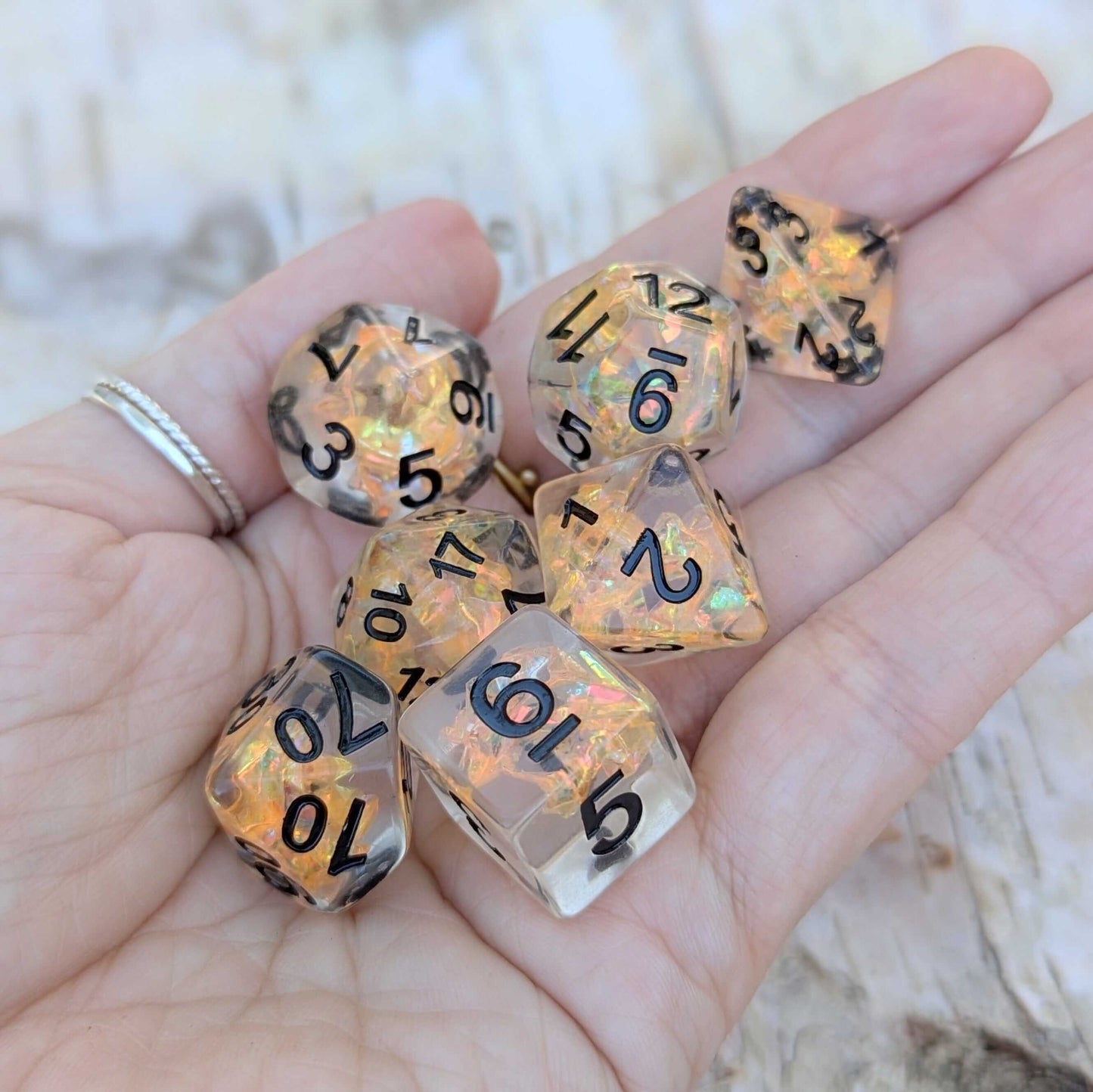"Hand holding Phoenix's Rebirth TTRPG dice set with orange iridescent cellophane and bold black numbers"