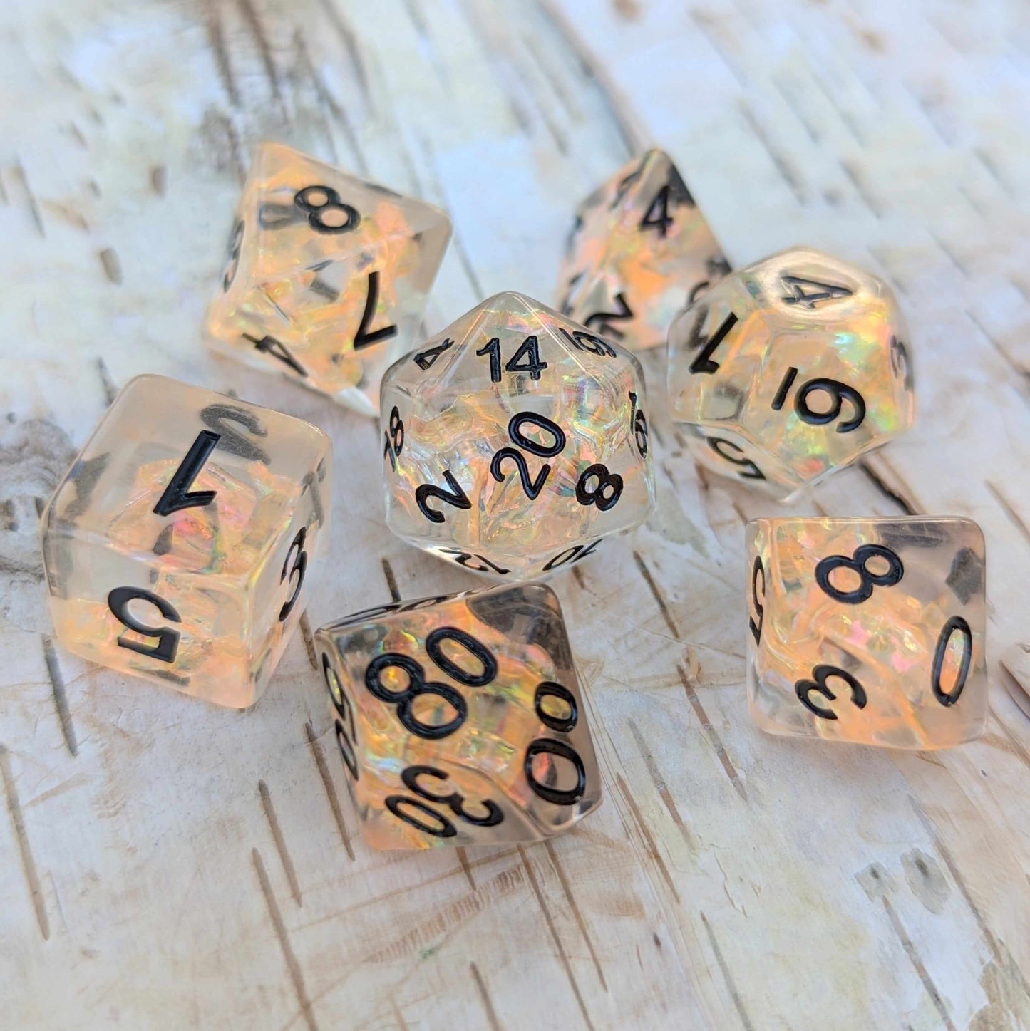 Phoenix's Rebirth TTRPG dice set with iridescent orange cellophane and black numbers on a wooden surface.