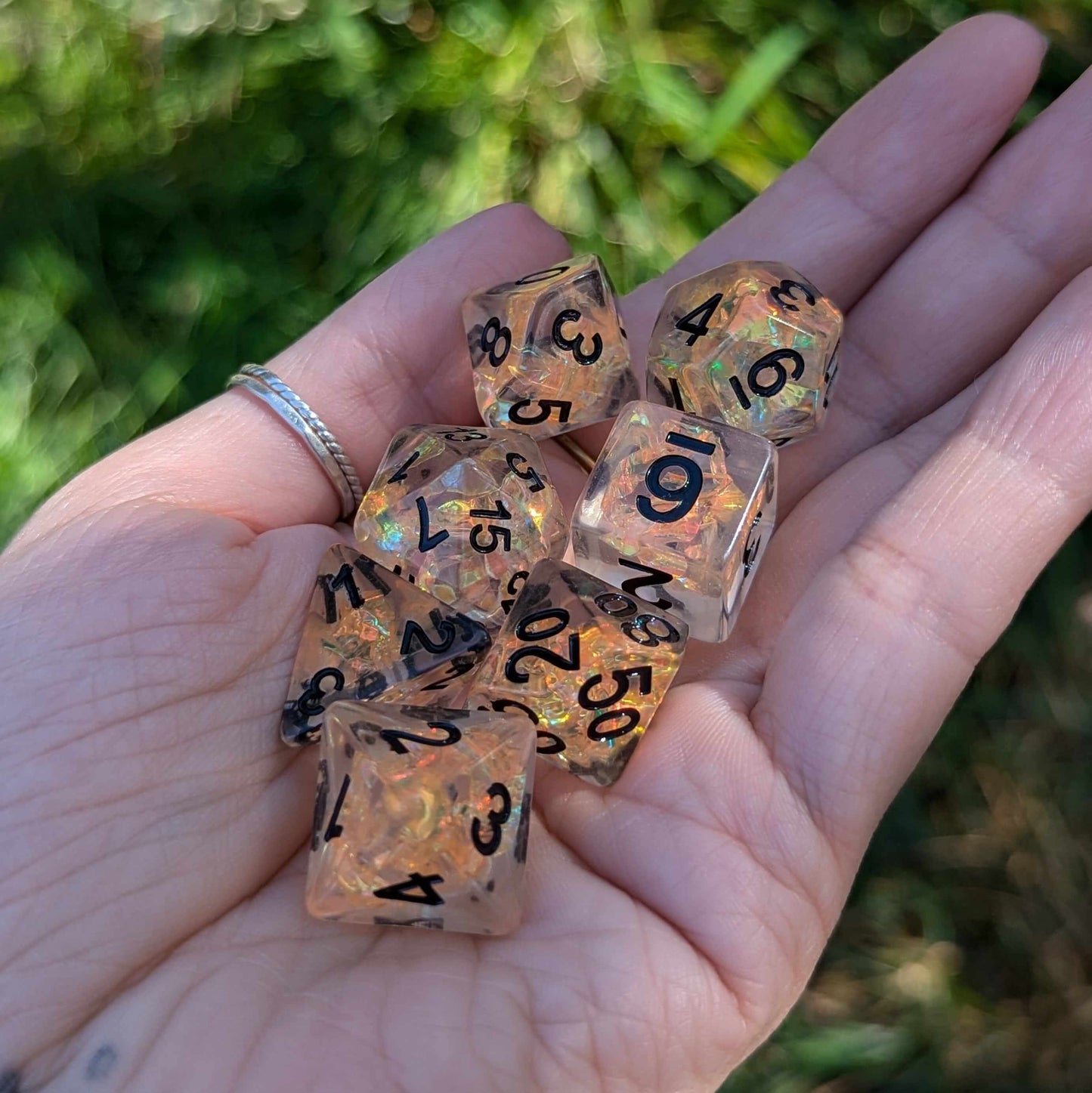 Clear resin dice with orange iridescent cellophane and black numbers, held in a hand.
