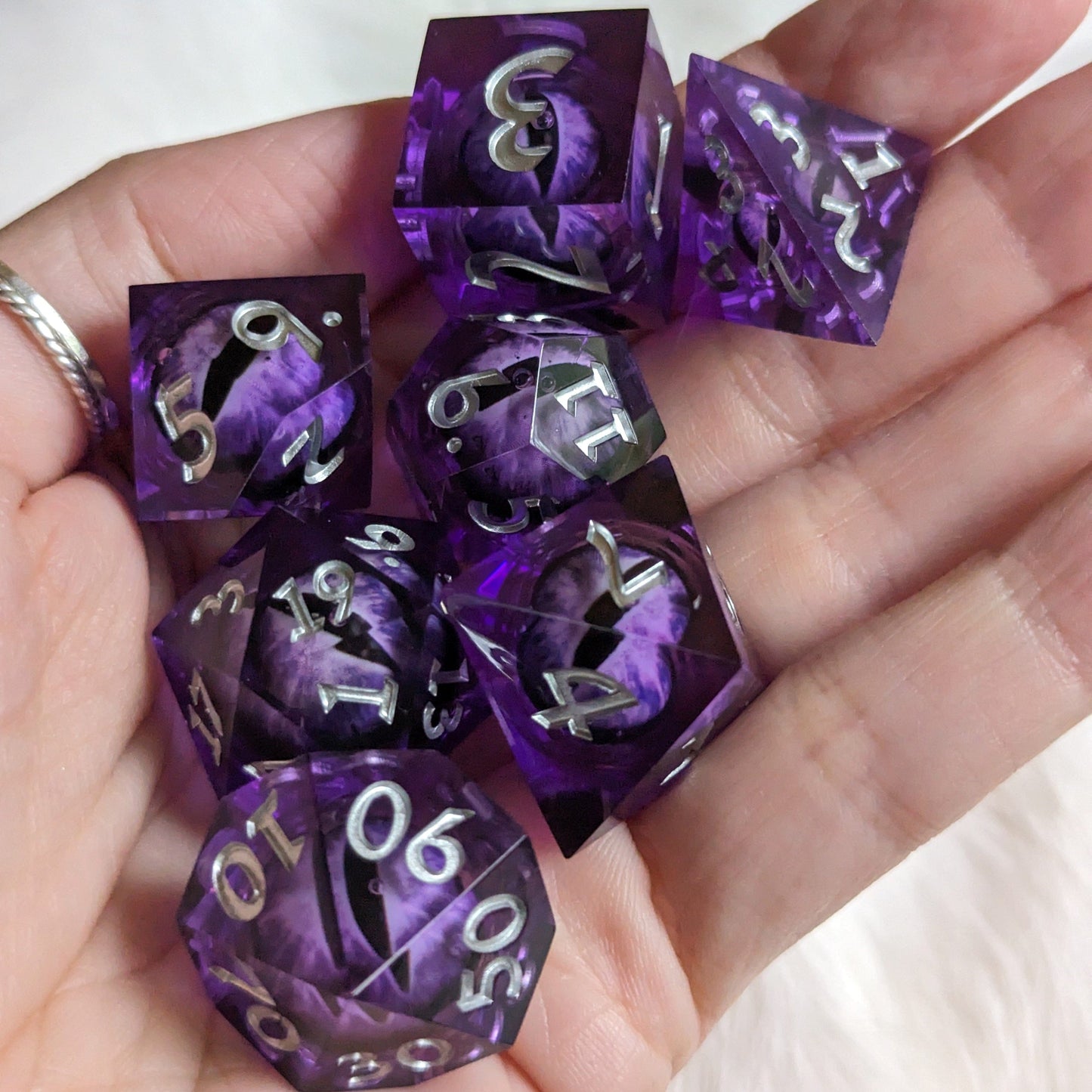 Purple moving eye liquid core sharp edge resin DnD dice set in hand, featuring 7 polyhedral dice for tabletop games.