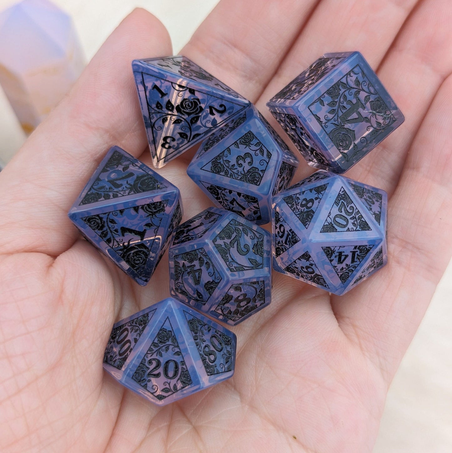 Hand holding a set of purple opalite dice engraved with black rose and vine designs, perfect for Dungeons & Dragons games.