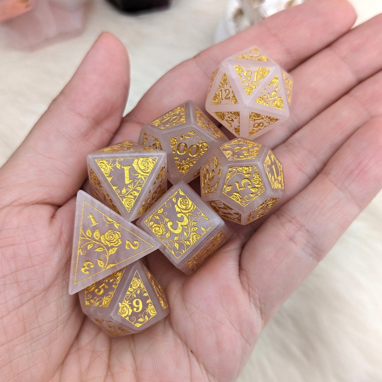 Hand holding Quartz of Roses Dice Set with gold rose and vine engravings on rose quartz, perfect for Dungeons & Dragons games.