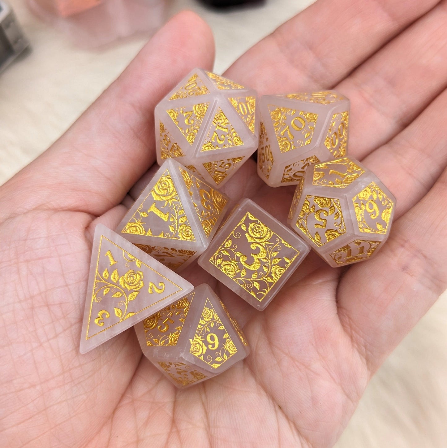 Rose quartz dice set with gold rose and vine designs for tabletop games in a hand.
