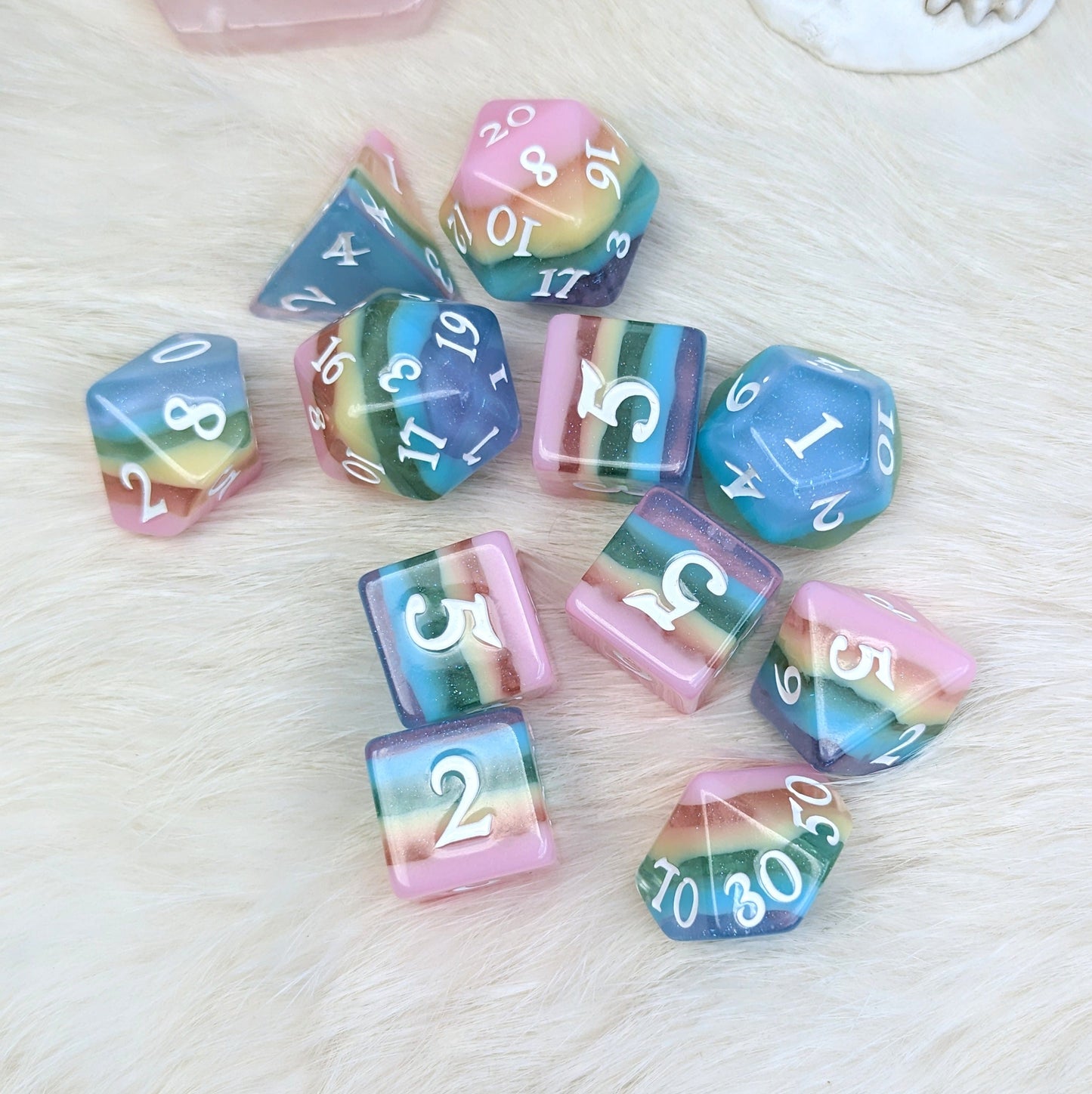 Pastel rainbow DND dice set with clear glitter layers, including D20 and D6 dice, on a textured surface. Fun and colorful gaming accessory.