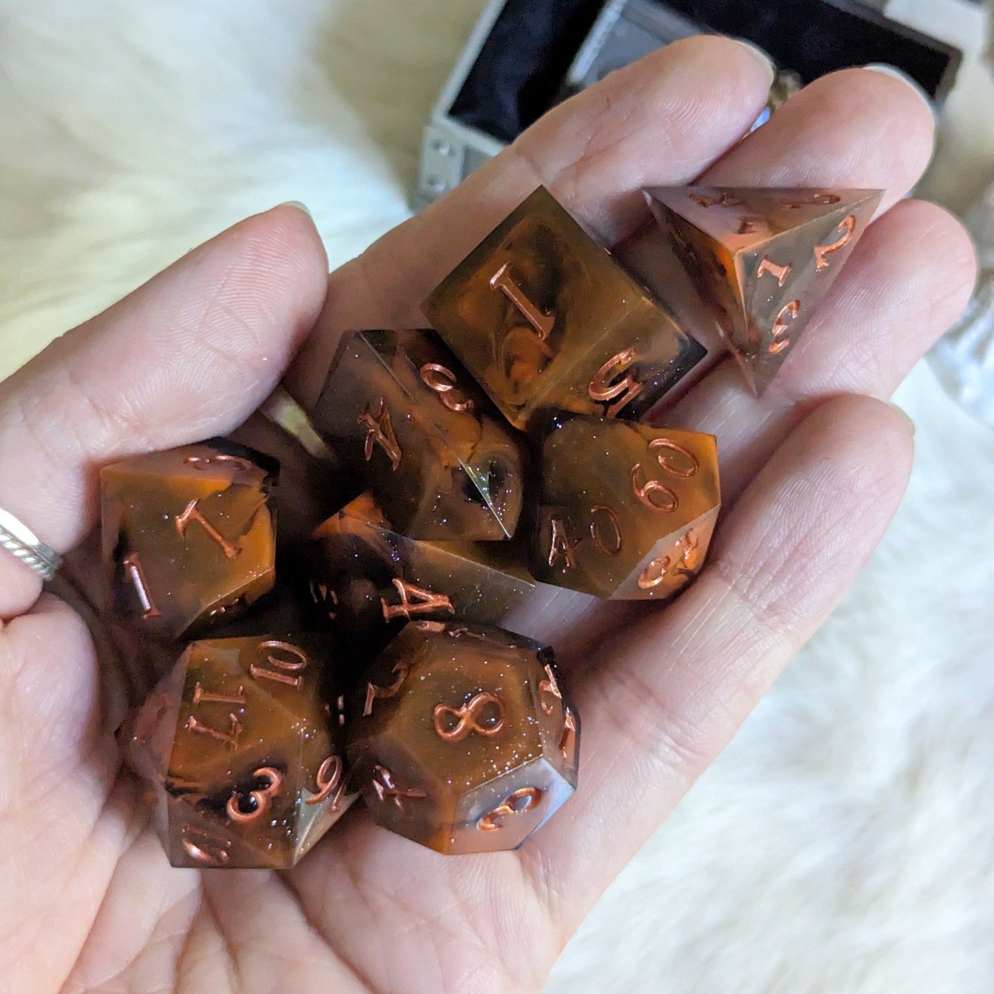 Hand holding Shadow and Flame DnD dice set; orange and black marble with copper font, 7 unique TTRPG dice.