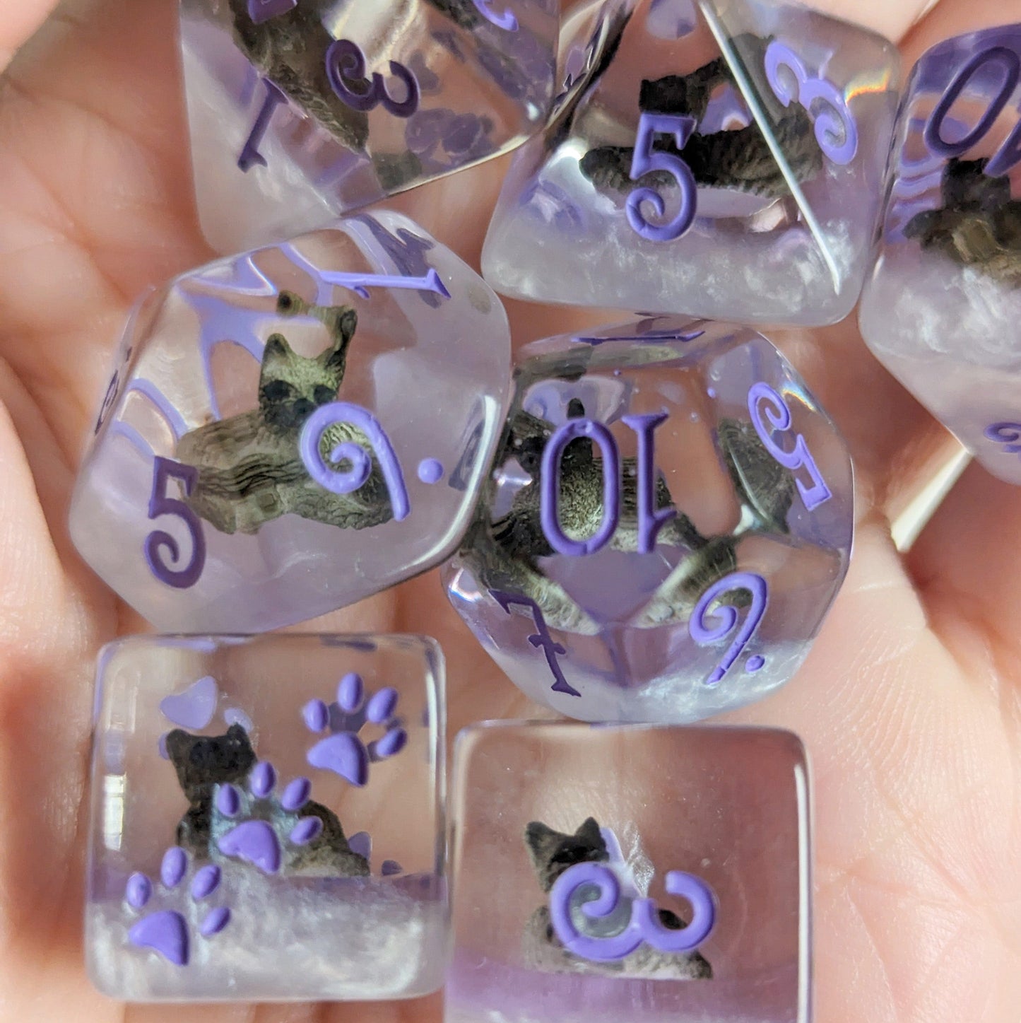 Sleepy Cat Dice Set with miniature cat designs, featuring eight polyhedral dice in clear resin with purple numbers and paw prints.