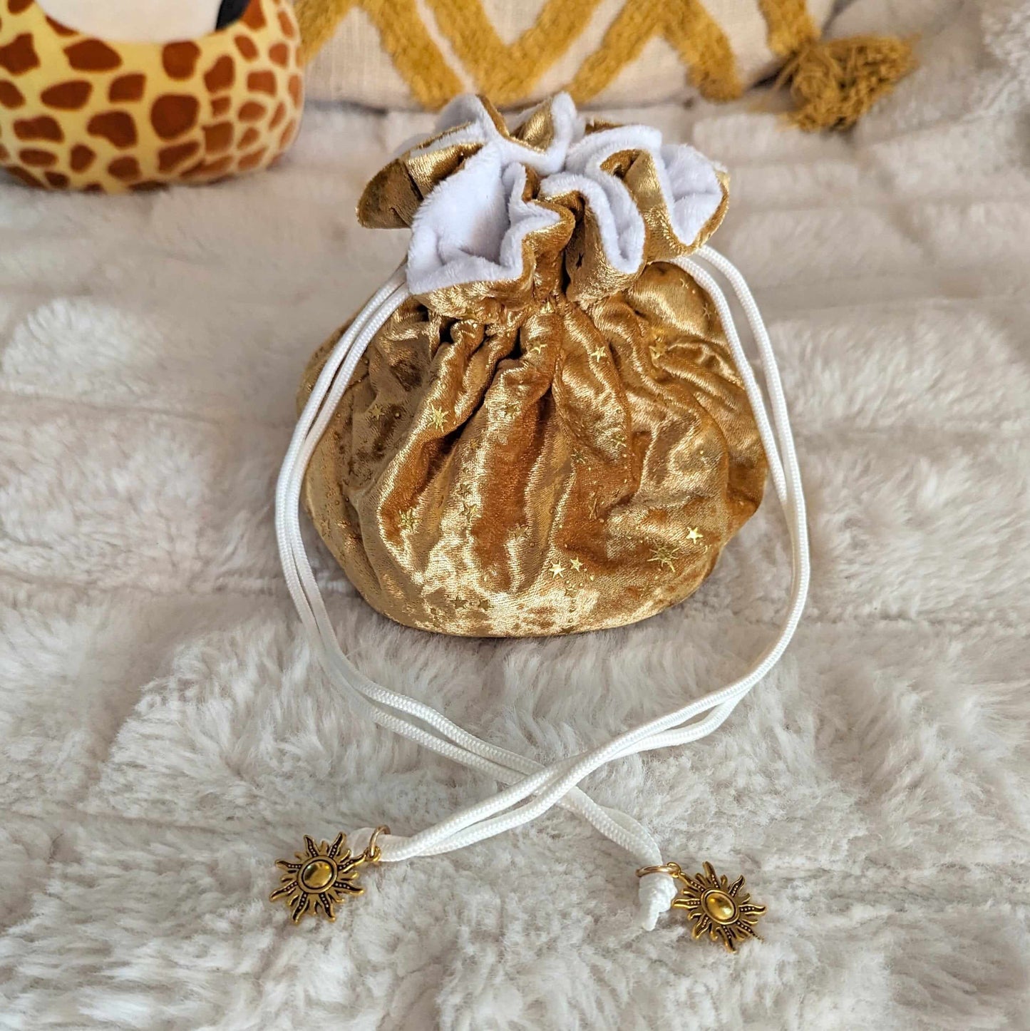 Gold velvet dice bag with starry pattern and sun charm drawstrings on plush white fabric background.