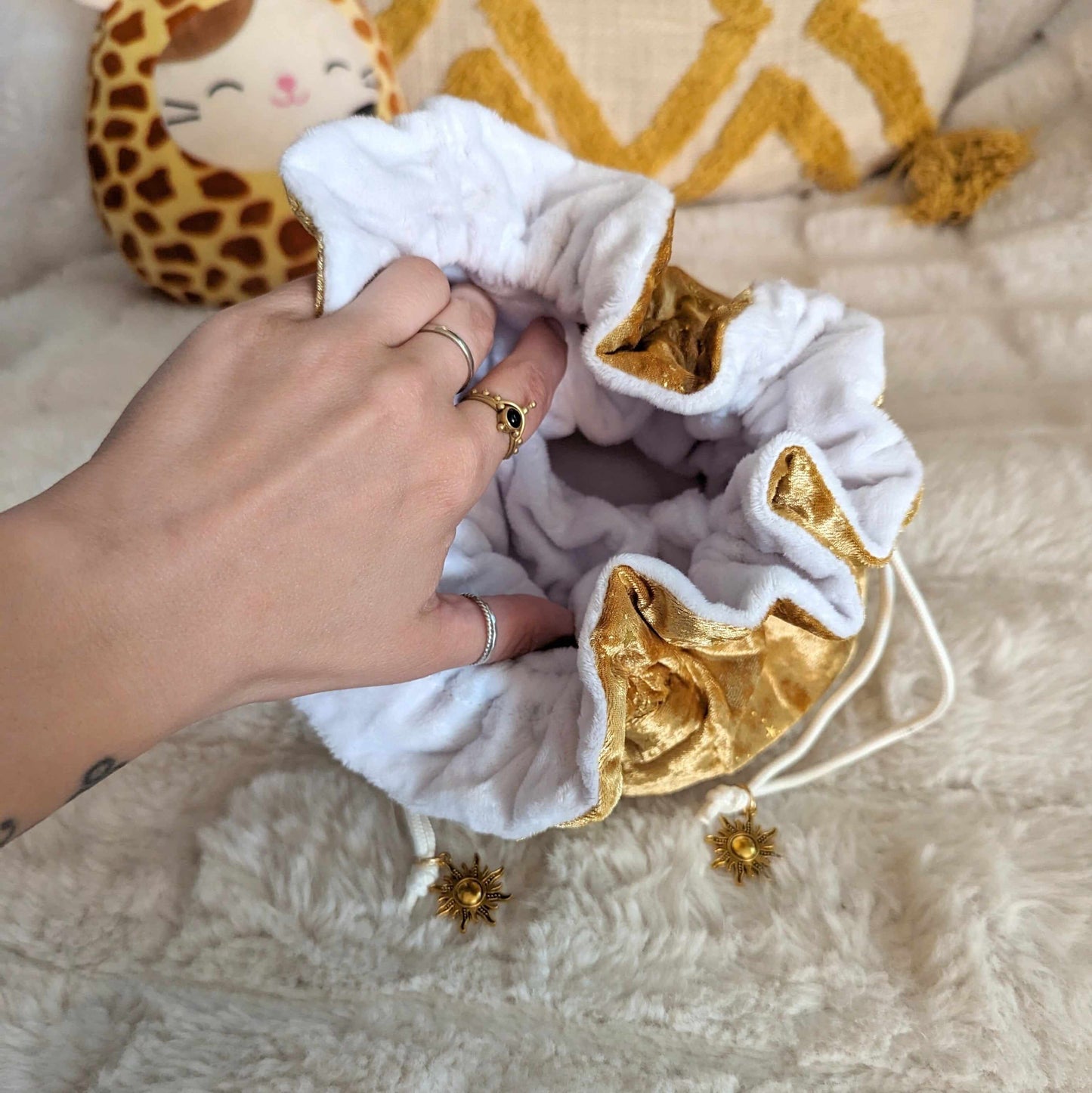 Hand opening luxurious gold and white dice bag with sun charm drawstrings, showcasing soft velvet and plush interior.