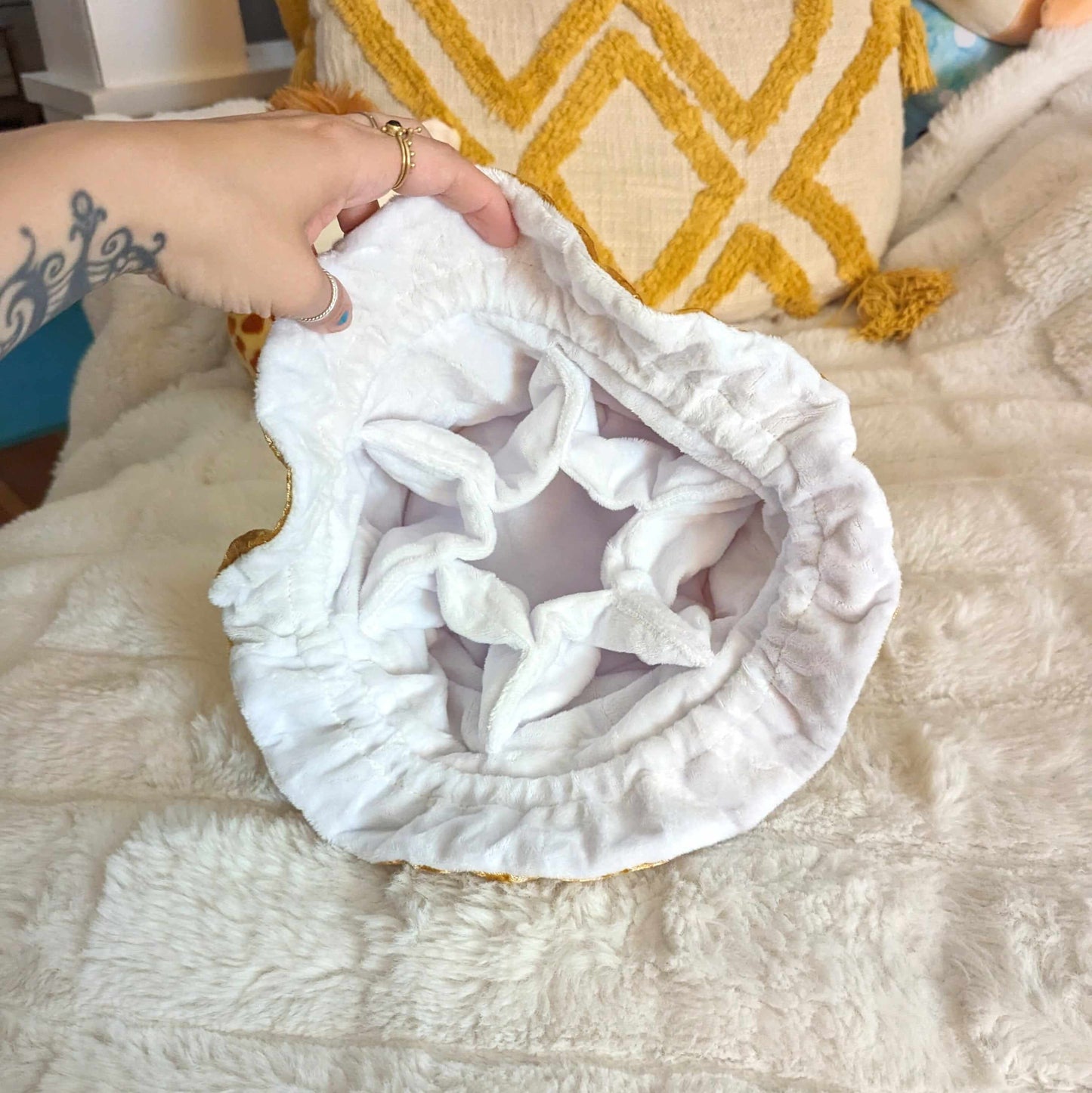 Person holding open the soft white interior of a gold velvet dice bag with multiple pockets on a plush white surface.