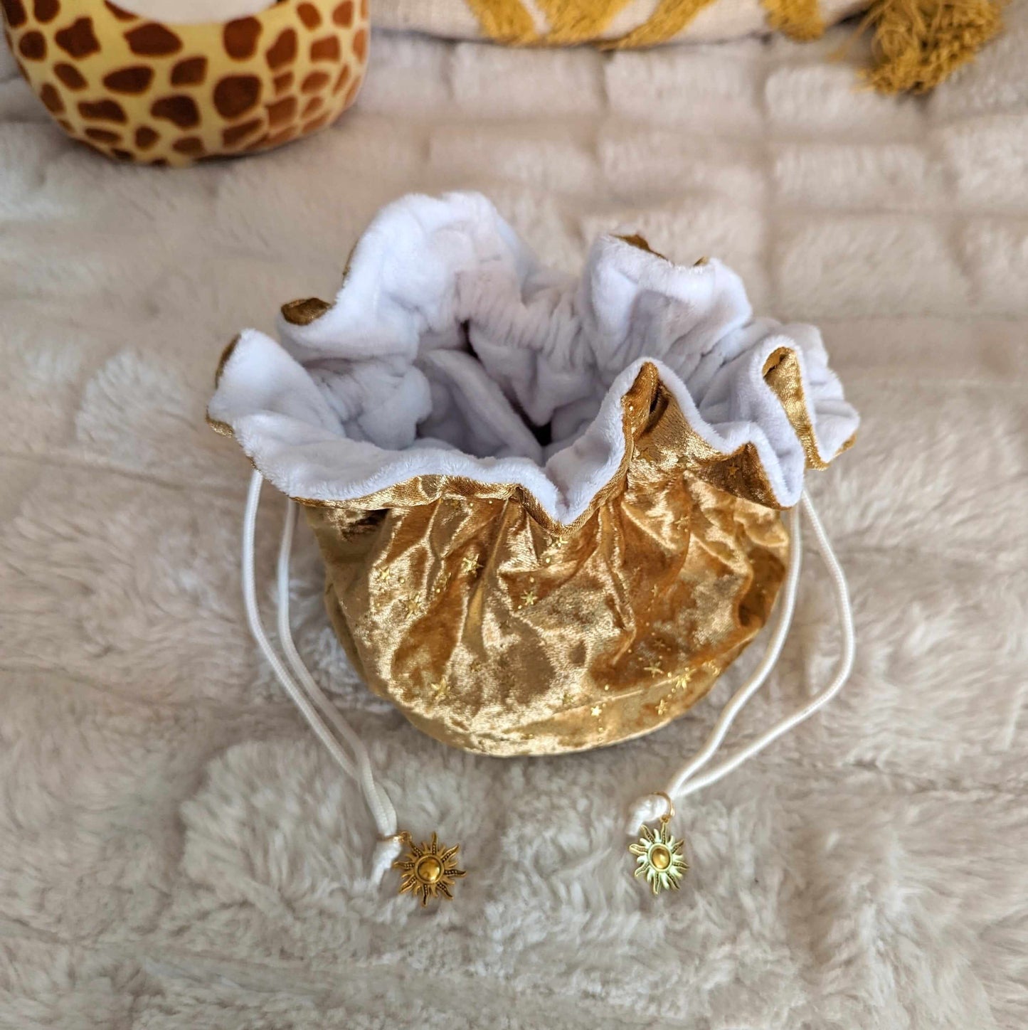 Luxurious gold dice bag with white plush lining and sun charm drawstrings on a soft, textured surface.