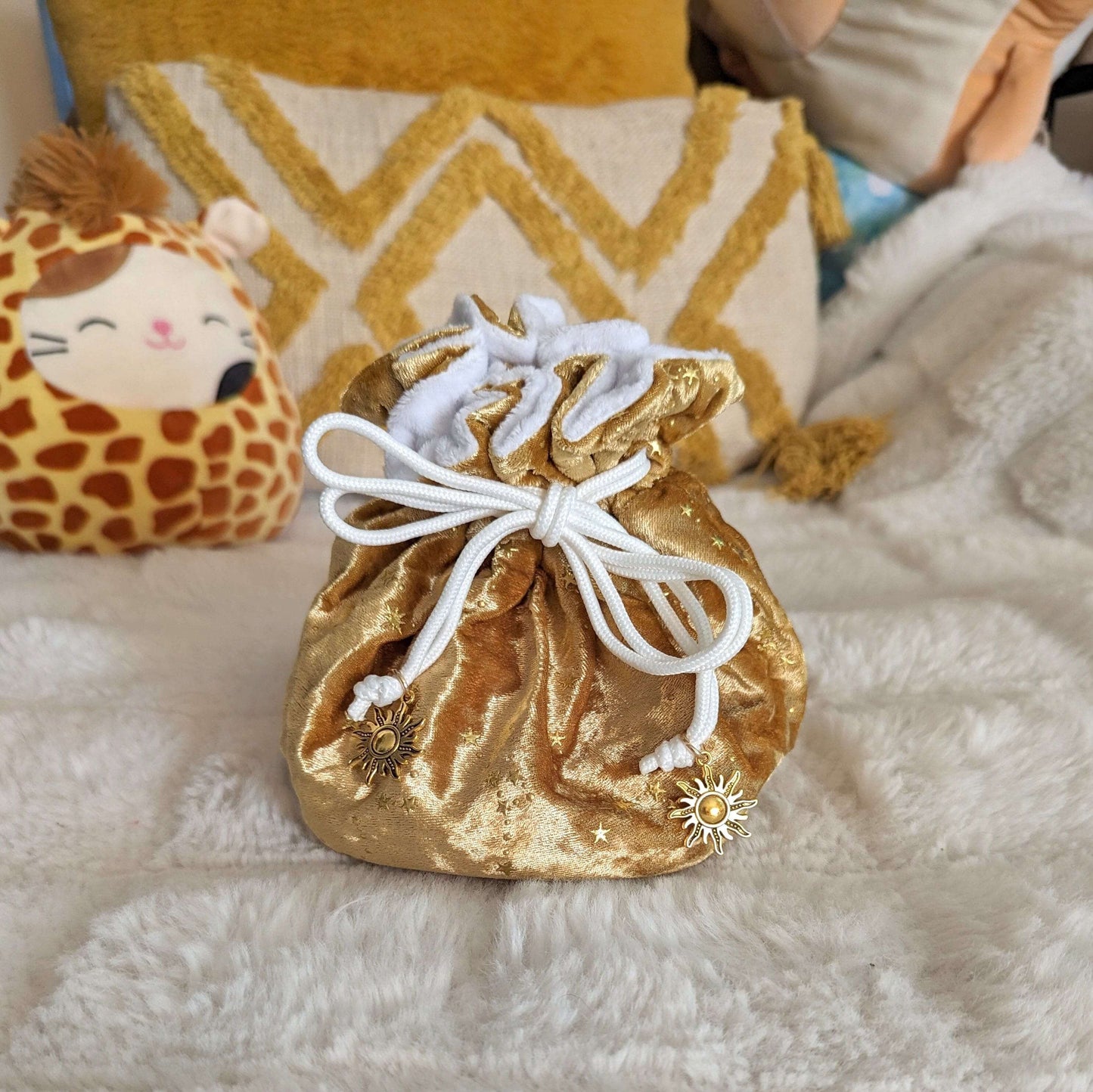 Luxurious gold velvet dice bag with white drawstrings and sun charms, featuring a plush interior, perfect for tabletop gaming.